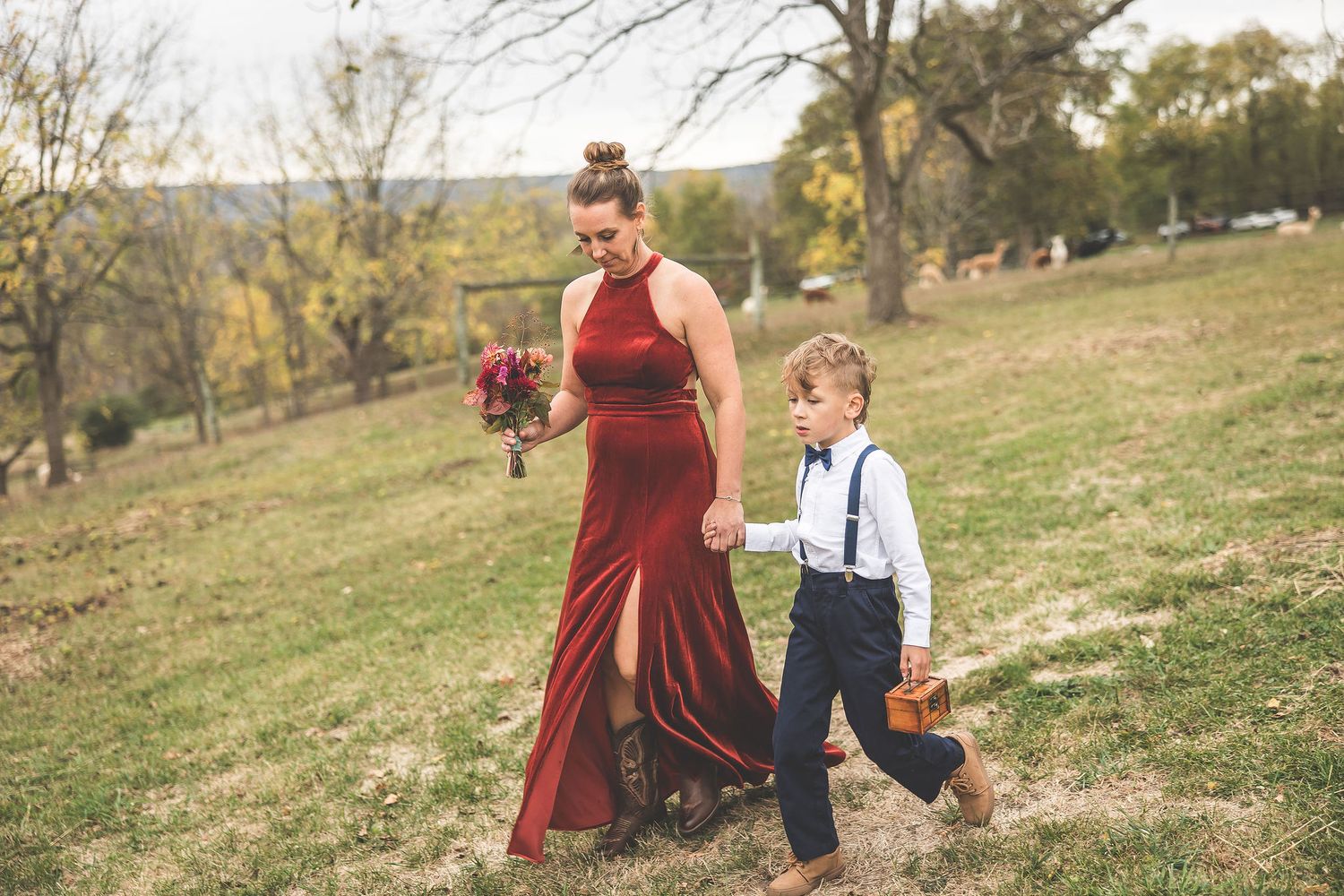Wedding party members walk and pose casually on grassy hillside during fall season.
