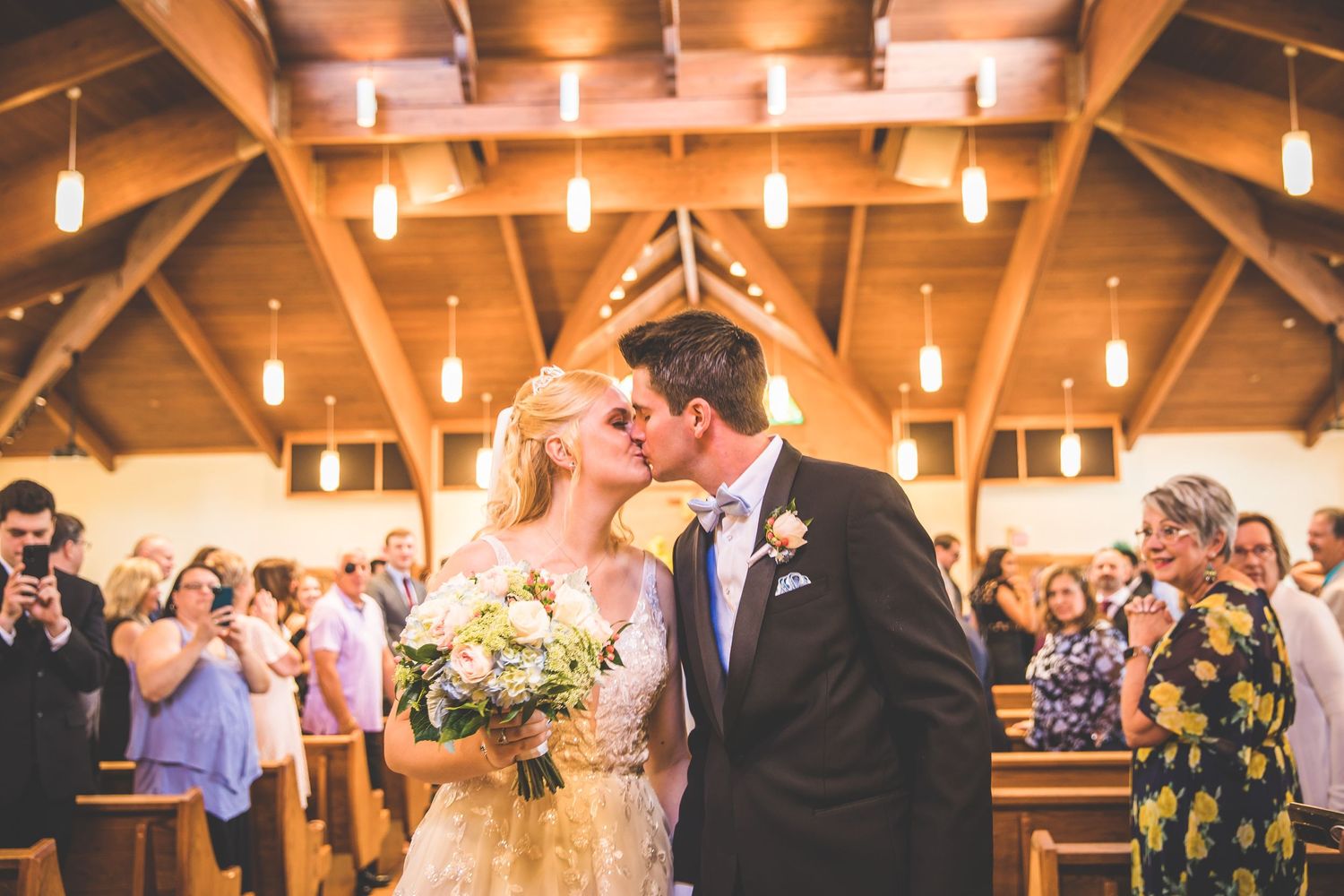 Warm-lit church wedding ceremony with wooden architecture and hanging pendant lights.