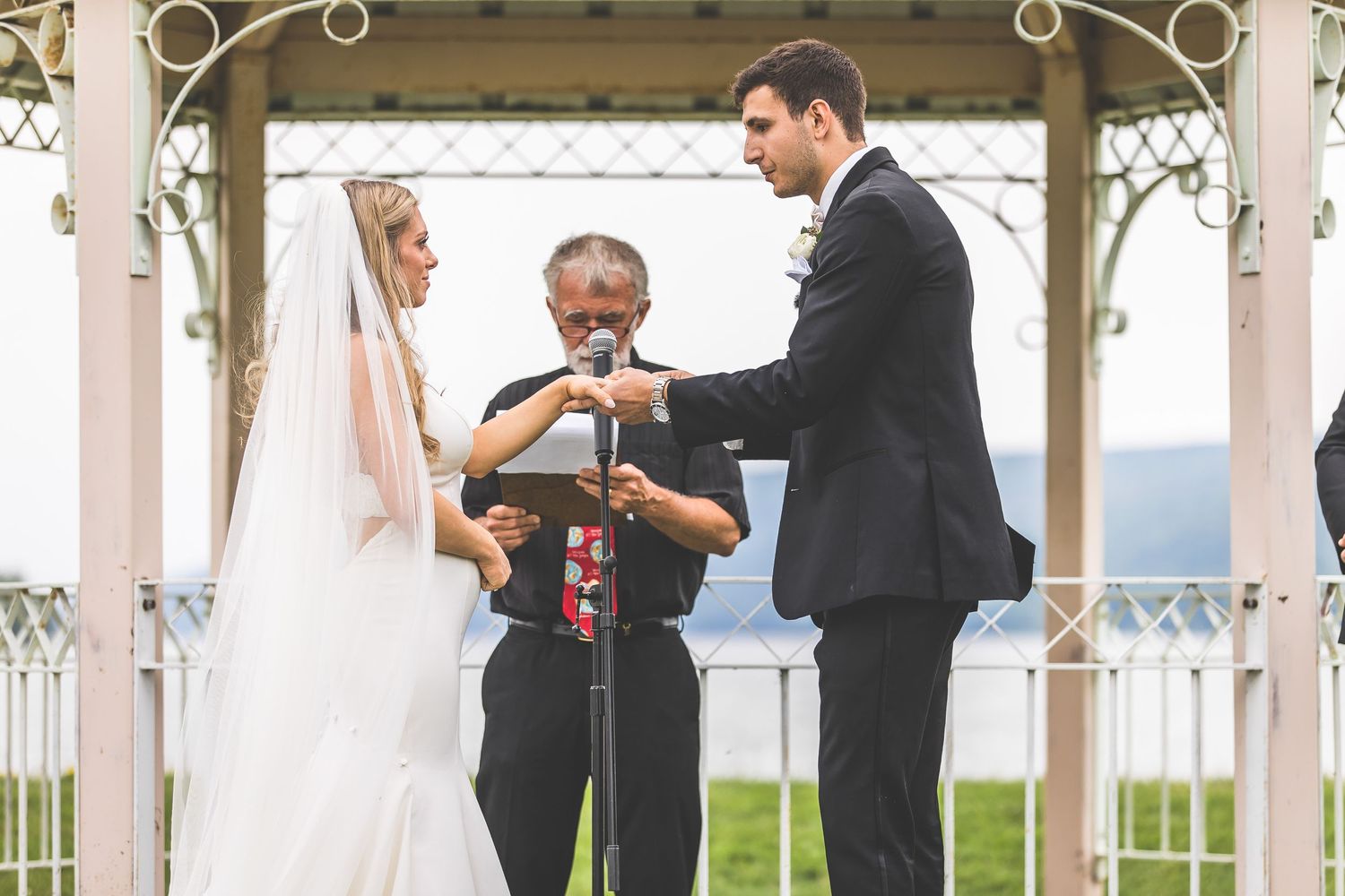Wedding ceremony in progress under decorative white gazebo with ornate trim details.