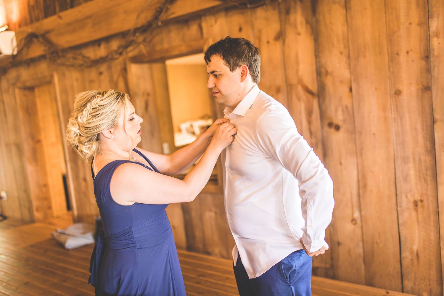 Wedding party members in blue dresses and formal wear posing inside a rustic barn.