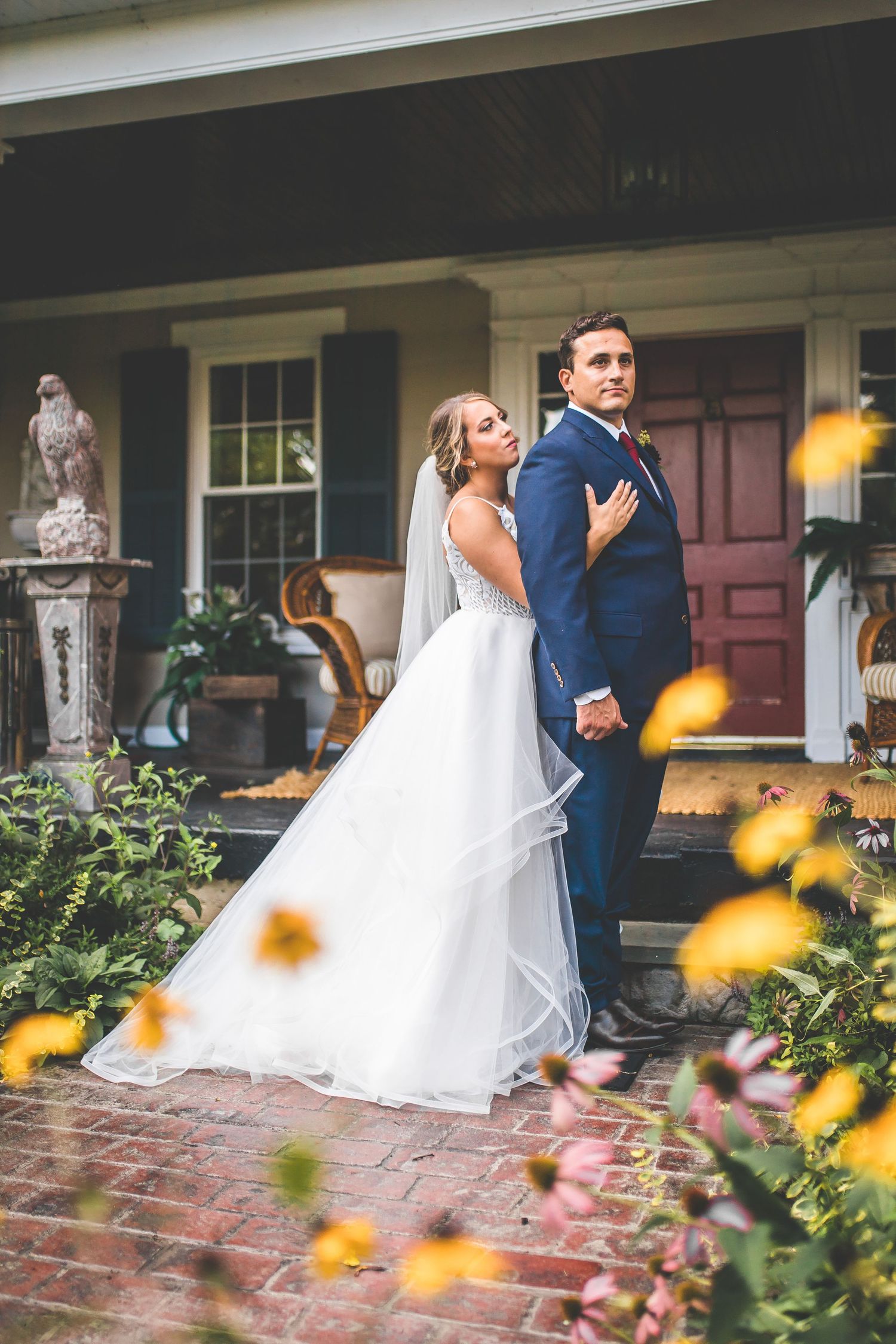 A couple shares a romantic moment on brick steps surrounded by yellow flowers and greenery.