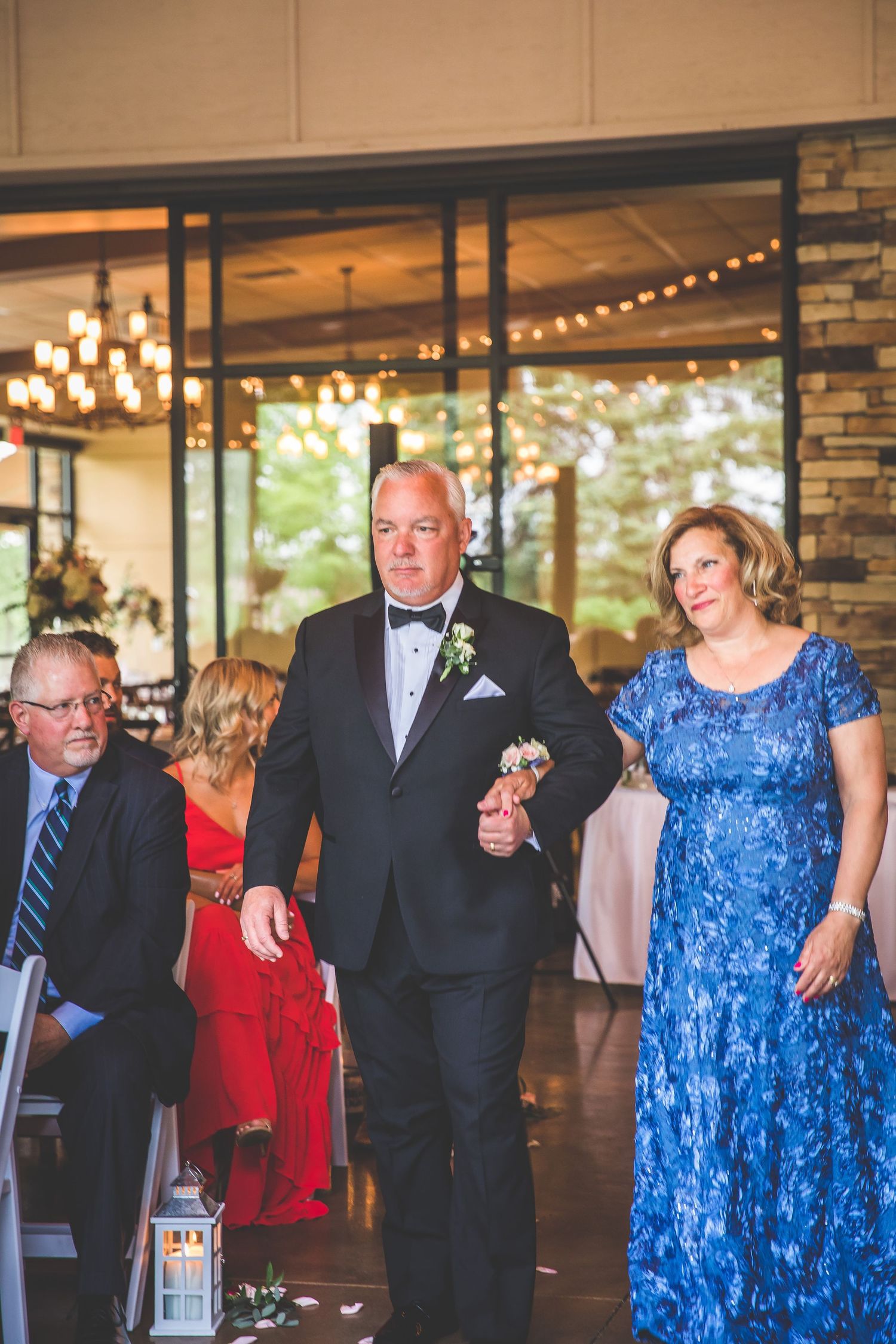 Wedding reception venue with stone walls, large windows, and guests in formal attire.