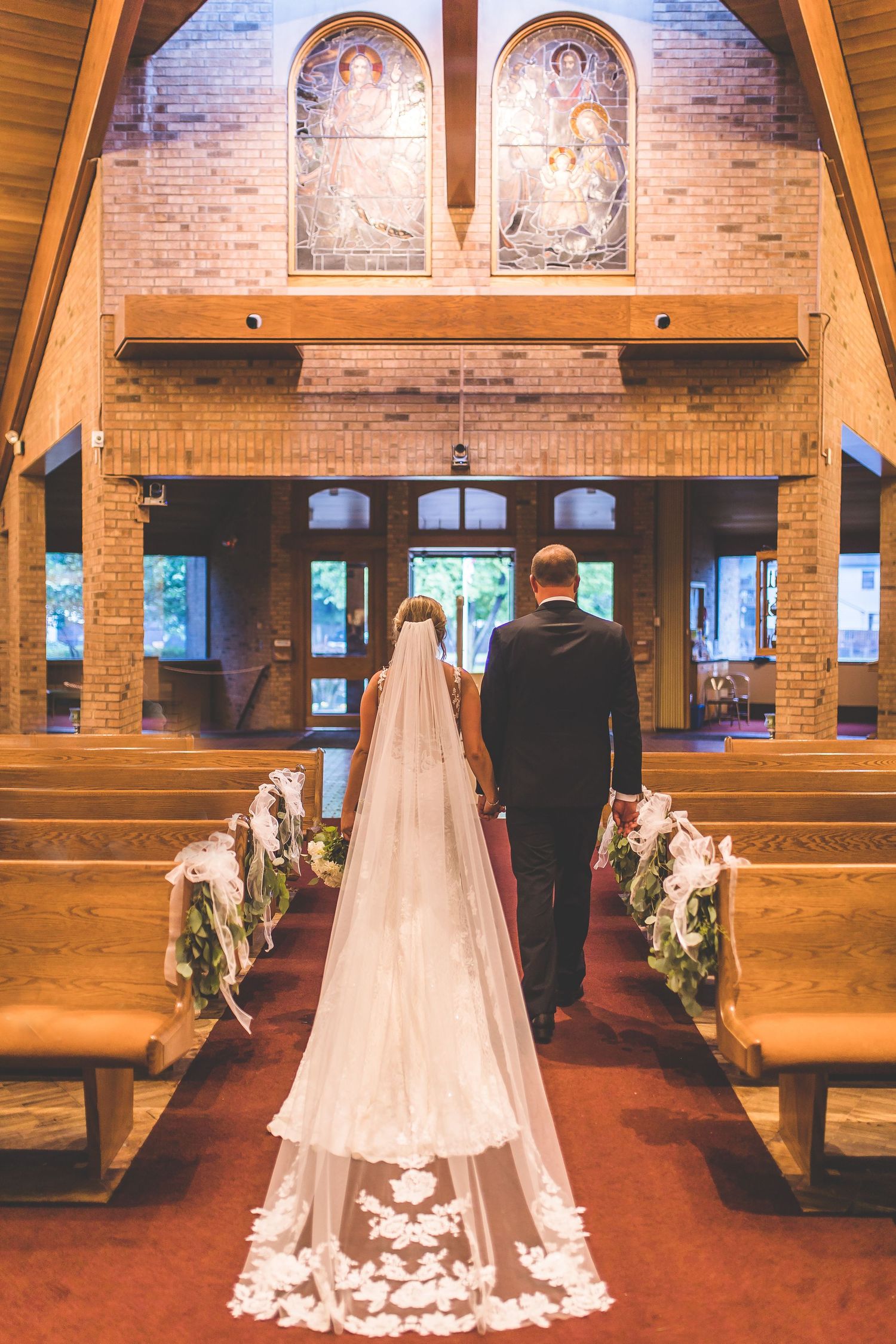 Church wedding ceremony with wooden pews and brick walls illuminated by natural light.
