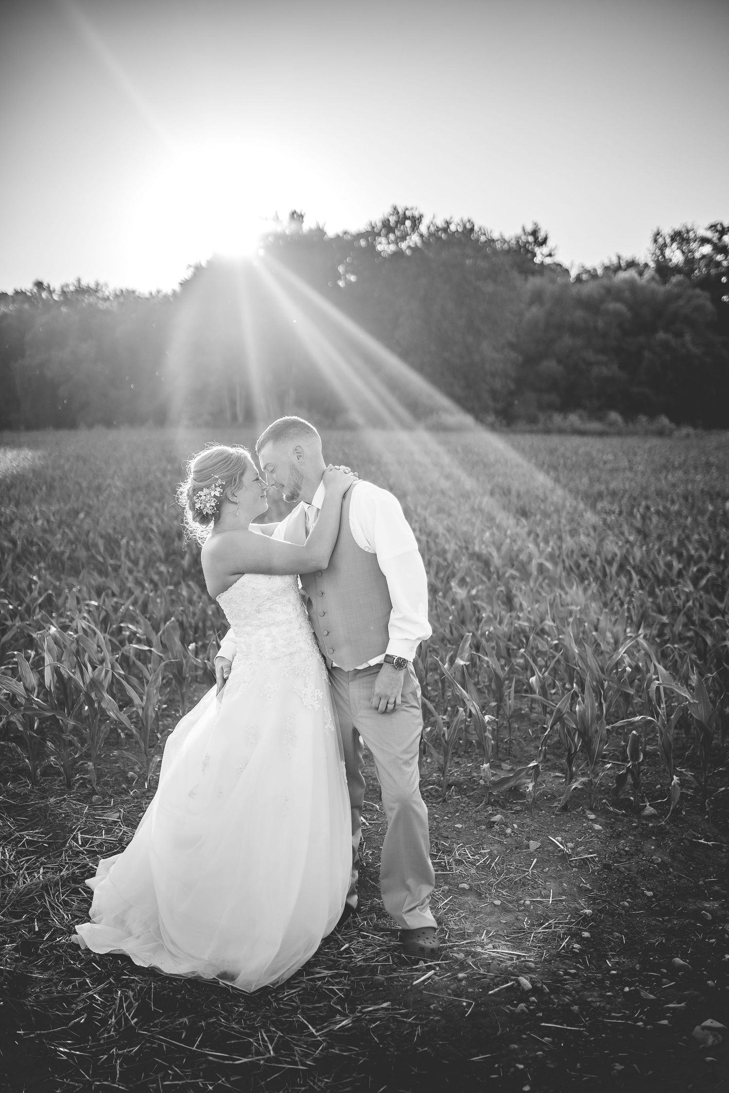 Black and white wedding portrait with dramatic sunbeams in a rural field.