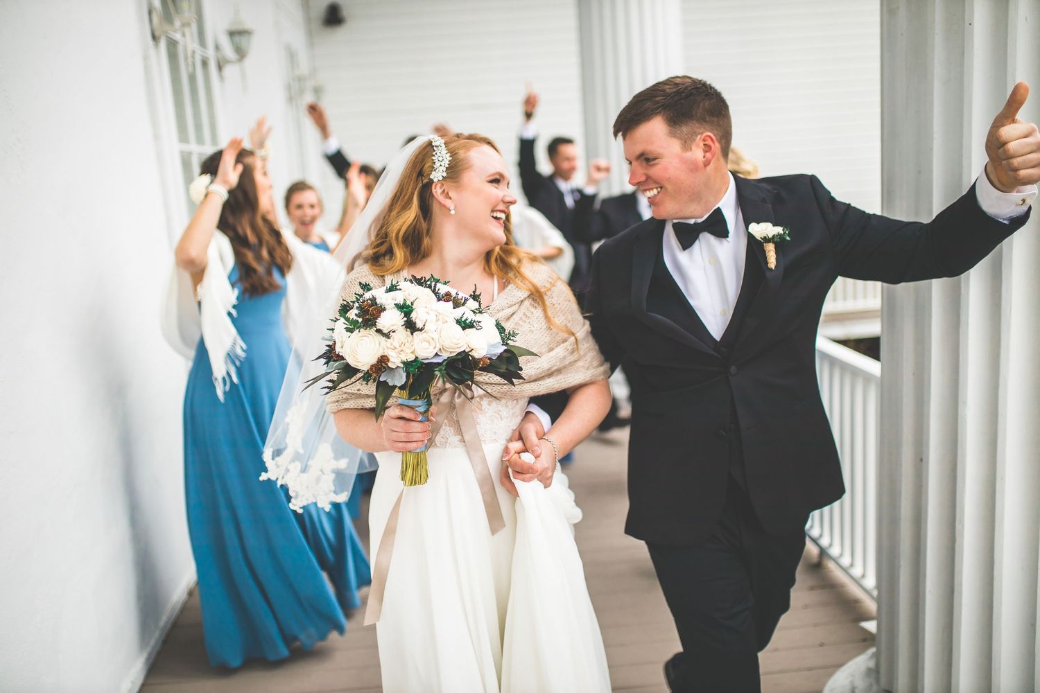 Wedding party celebrates with raised arms on a columned white porch.