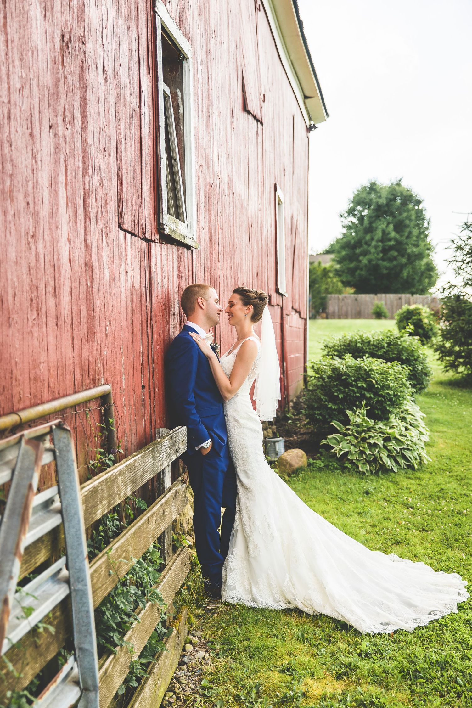 A wedding couple shares an intimate moment against a rustic red barn backdrop.