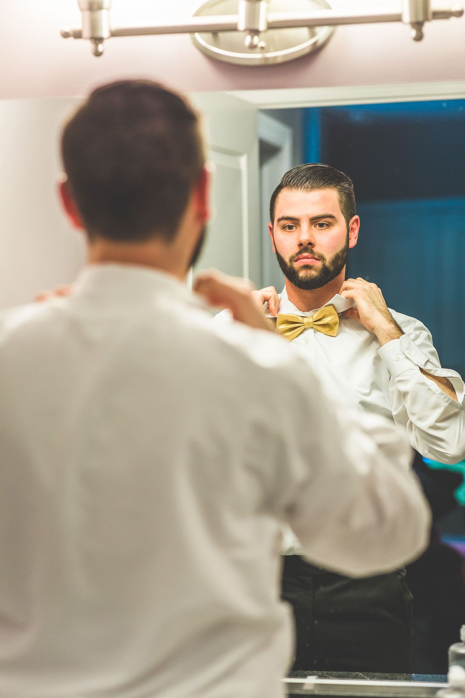 Man adjusting a yellow bow tie while looking in the mirror during wedding preparations.