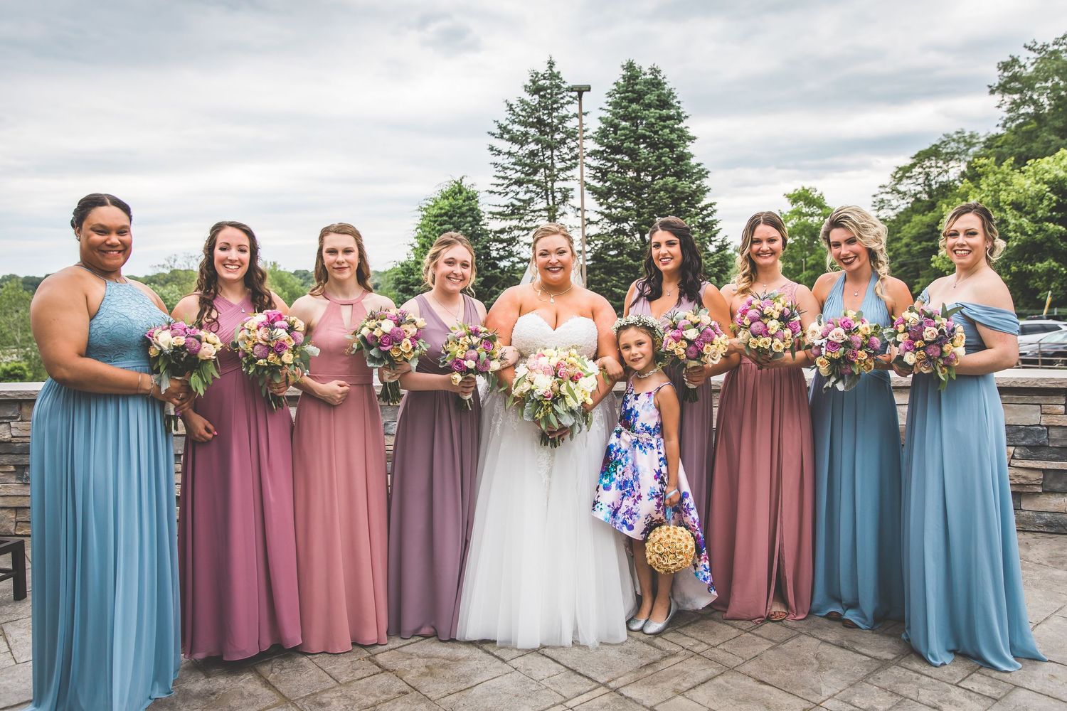 Bridal party in coordinating blue and mauve dresses posing outdoors.
