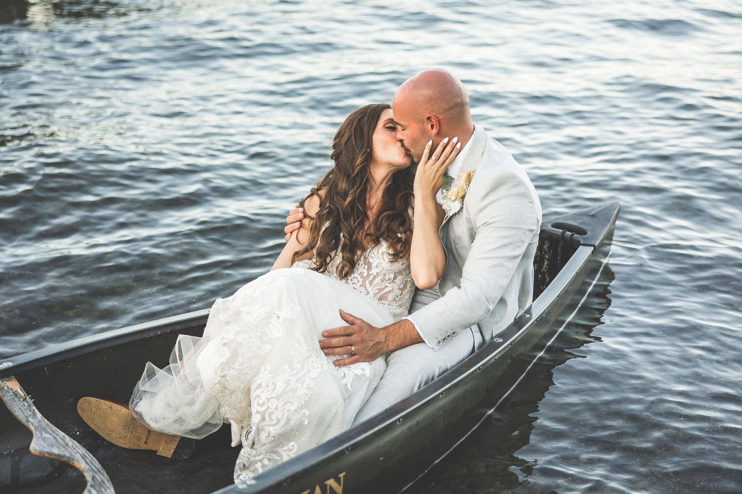 A romantic wedding couple shares an intimate moment while sitting in a boat on the water.