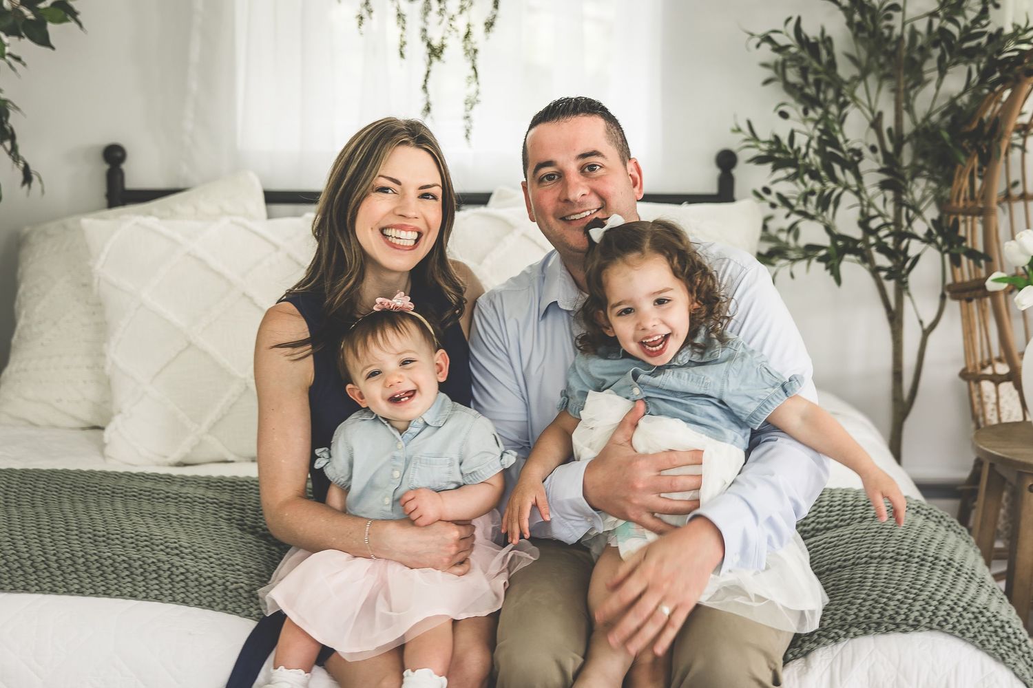 Happy family with young children sitting together on gray couch surrounded by indoor plants.