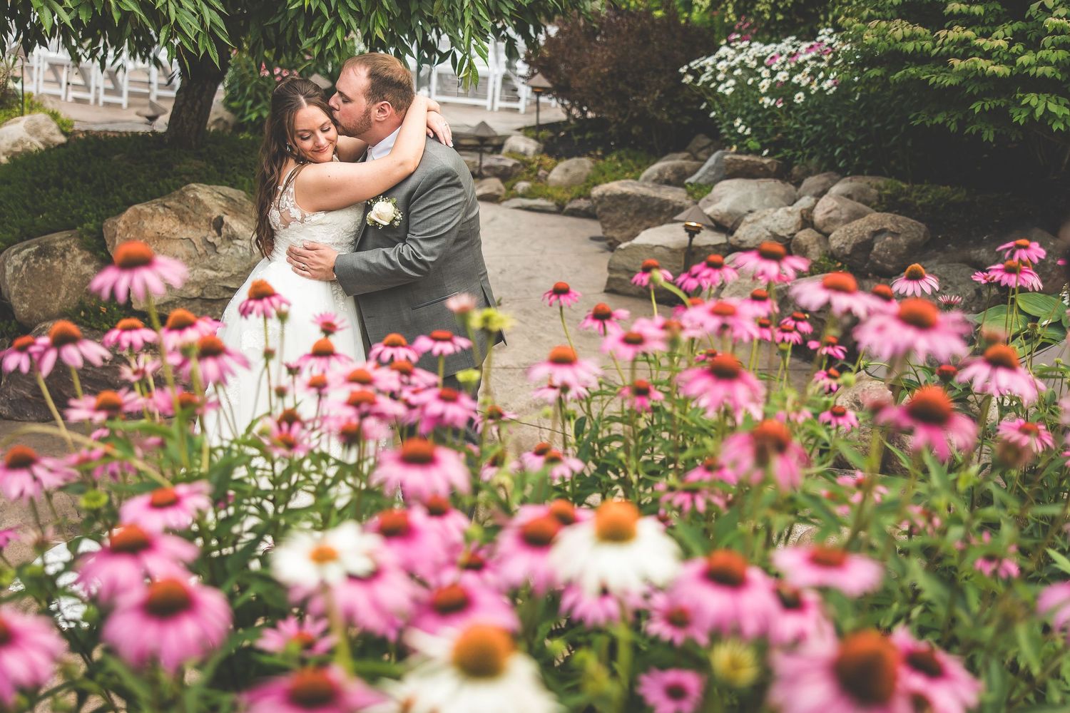 Wedding couple embracing in garden with pink coneflowers blooming in foreground.