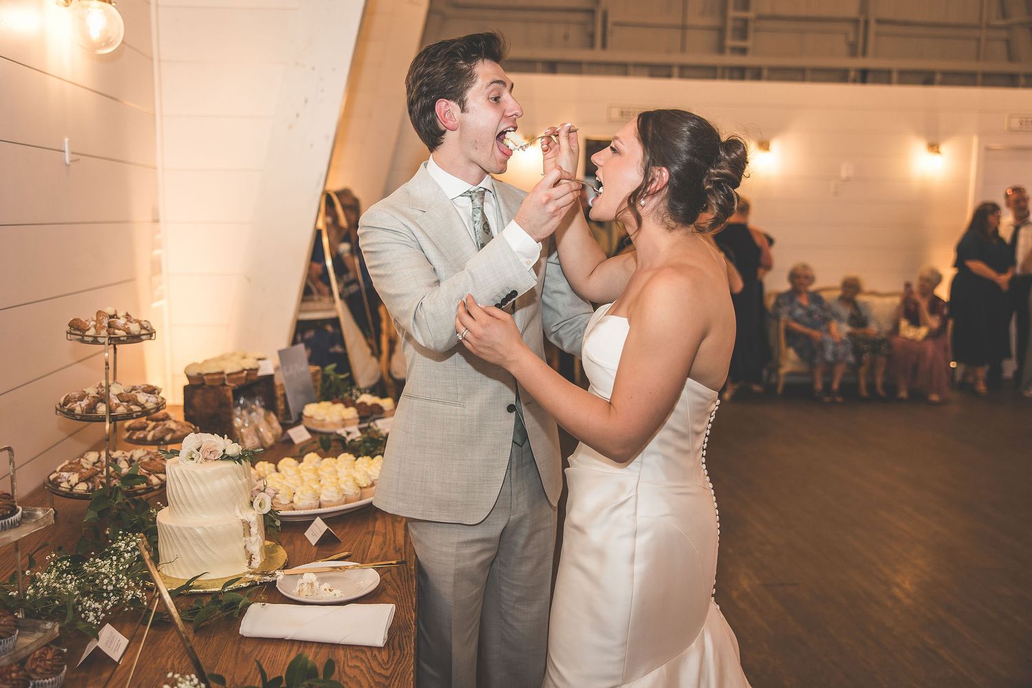 Wedding cake cutting ceremony in a rustic indoor venue with warm lighting.