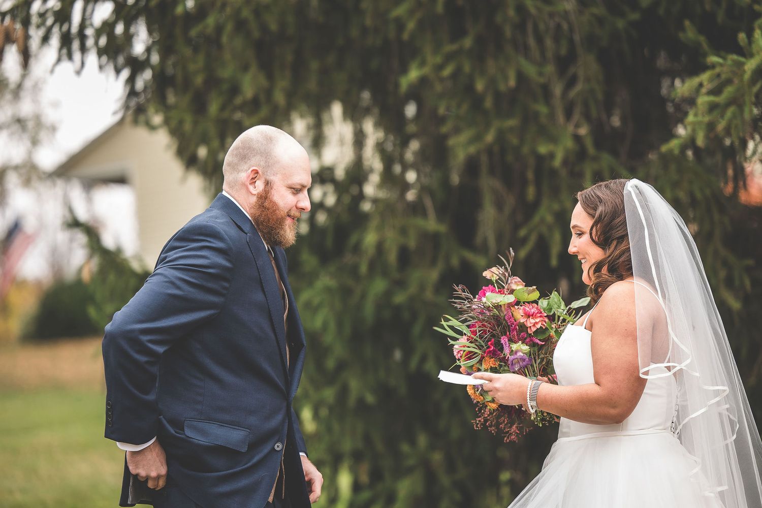 A bride holds a vibrant autumn bouquet while exchanging vows with her partner outdoors.