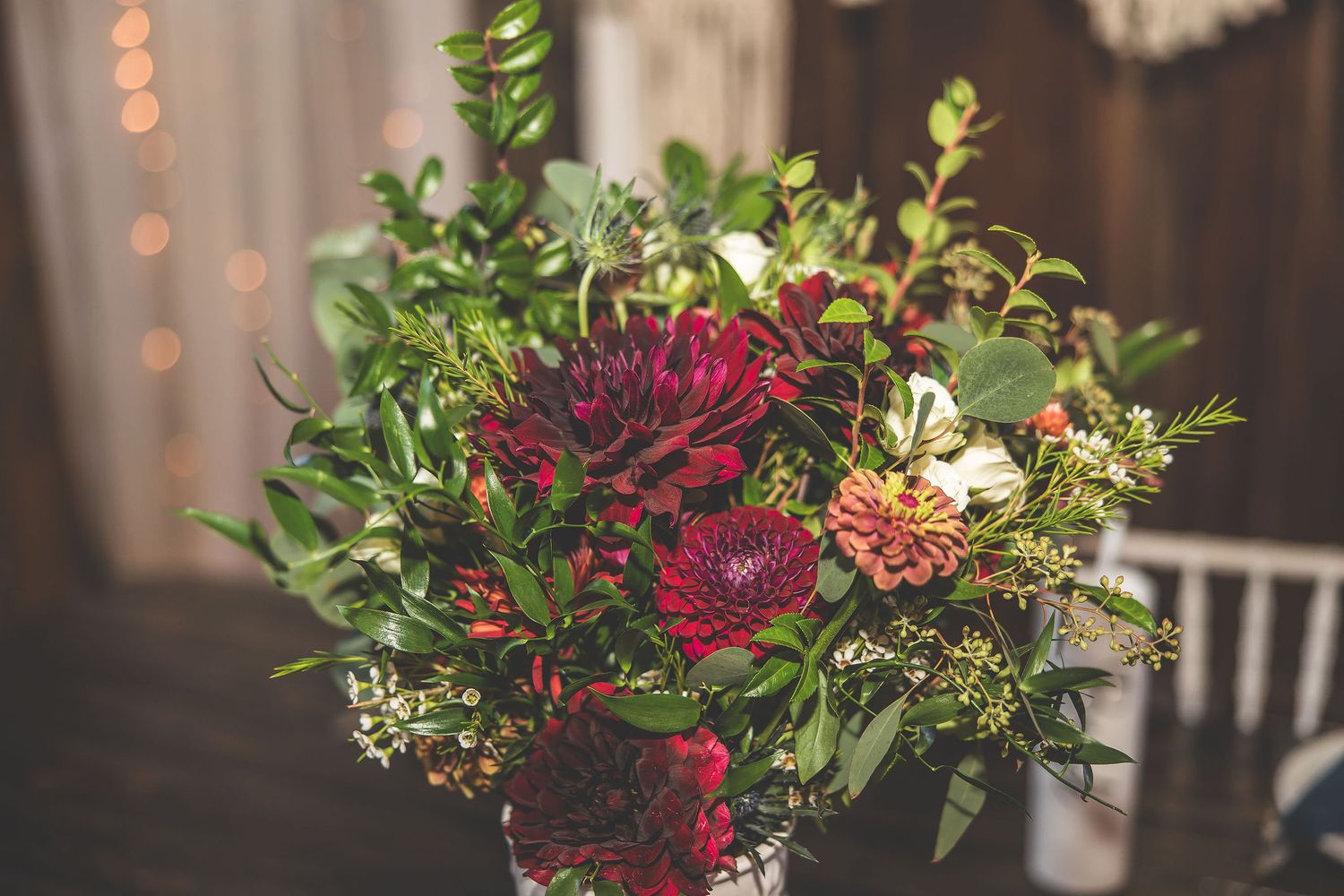 Deep burgundy and pink floral arrangements with greenery displayed at a wedding reception.