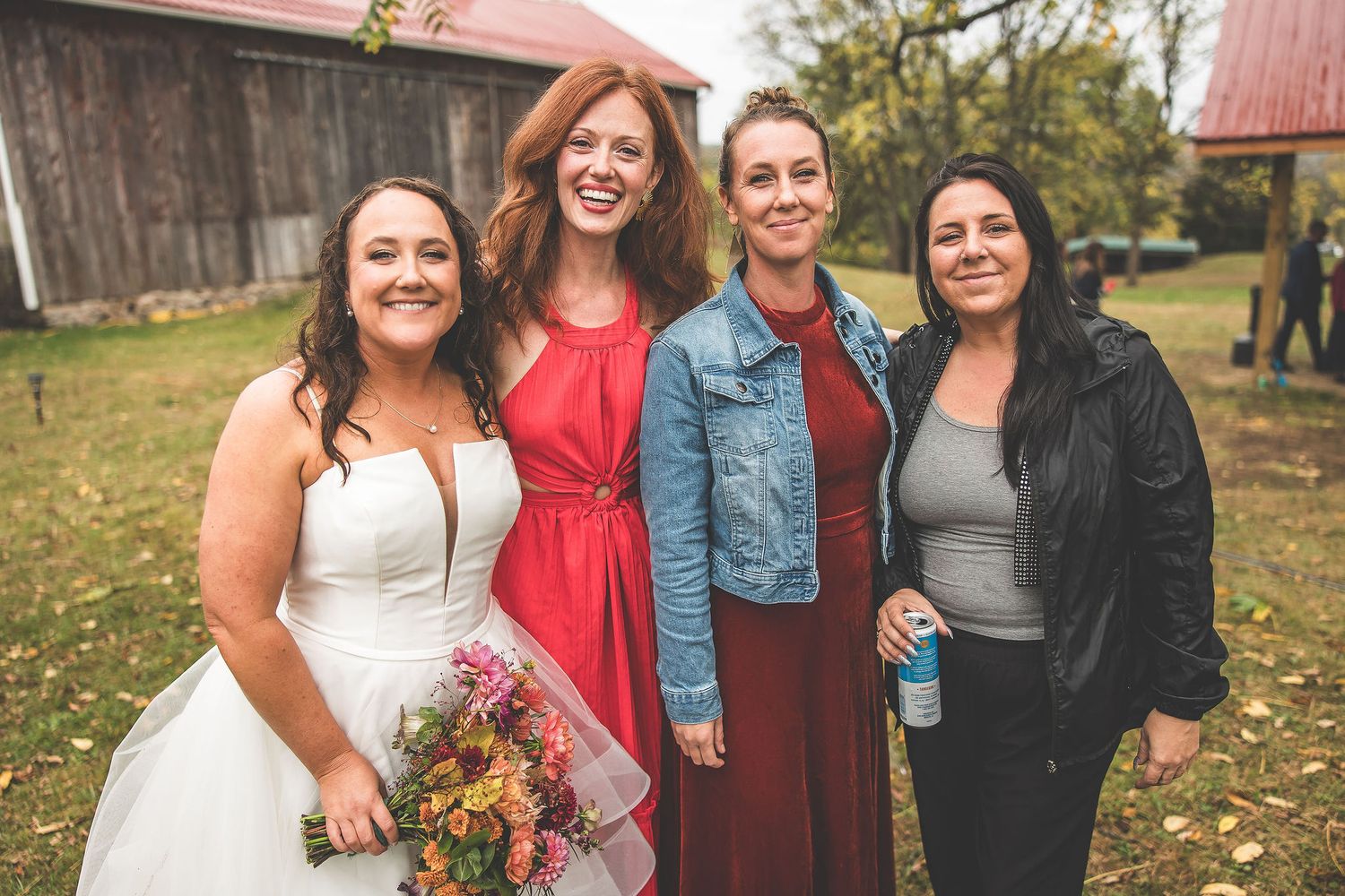 Bridal party in purple dresses and red accents poses together outdoors during fall wedding celebration.