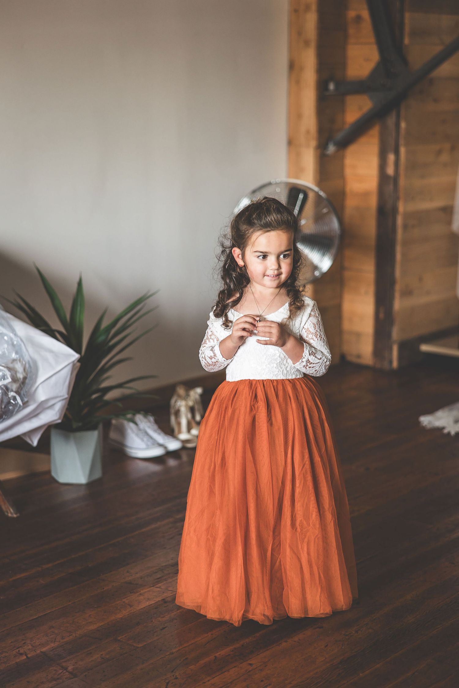 Young attendant in white and orange dress stands in rustic venue setting.