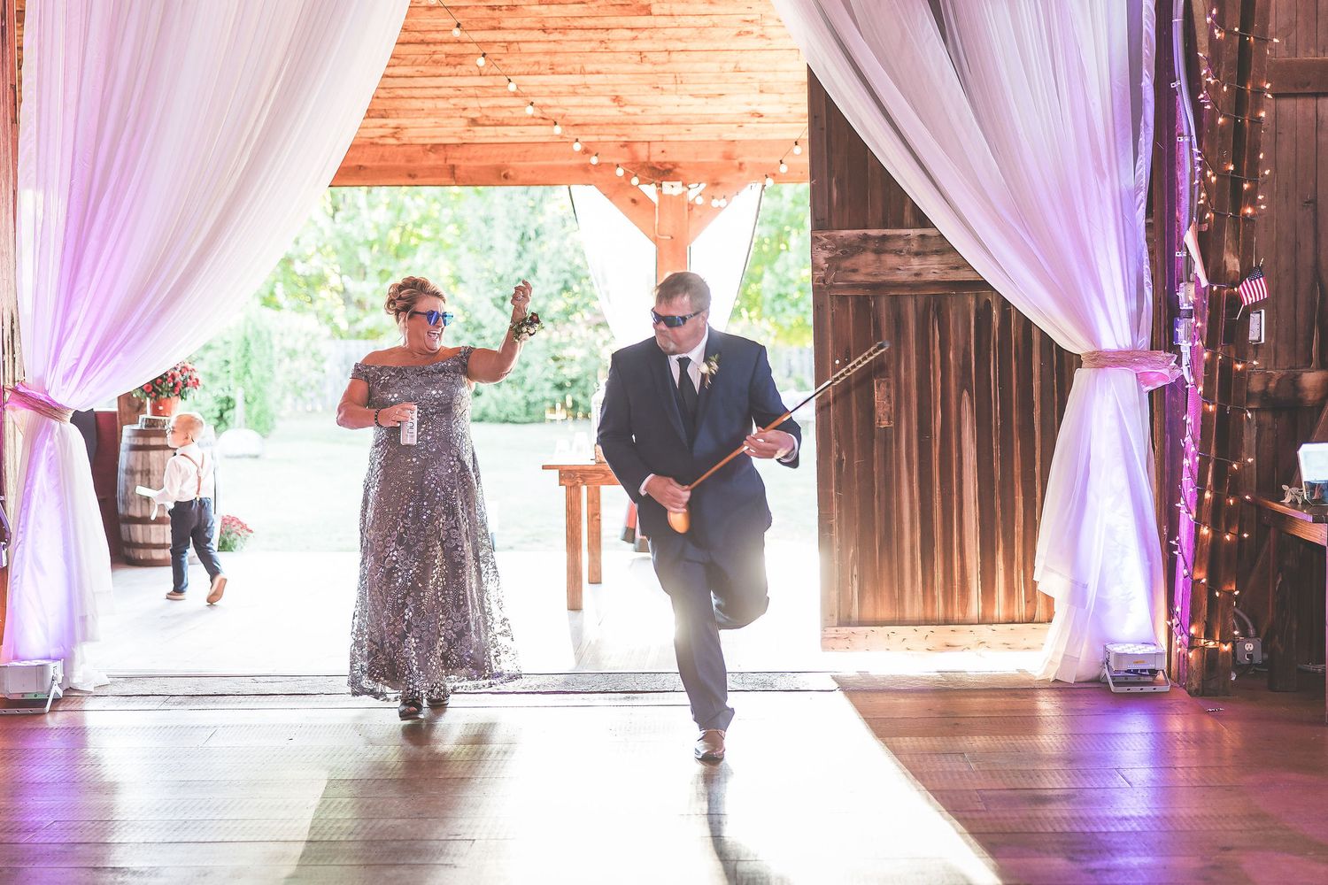 Couple dancing together during first dance at rustic barn wedding reception with purple lighting and white drapes.