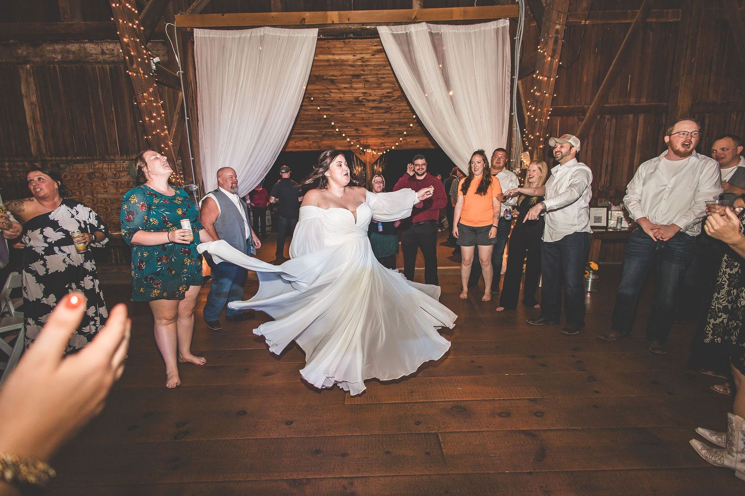A dancer twirls in a flowing white dress as guests watch in a rustic barn venue.