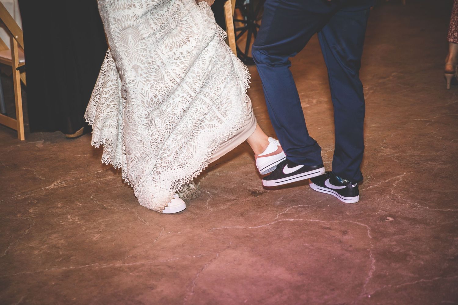 Wedding guests dance and celebrate on a rustic wooden dance floor under warm lighting.