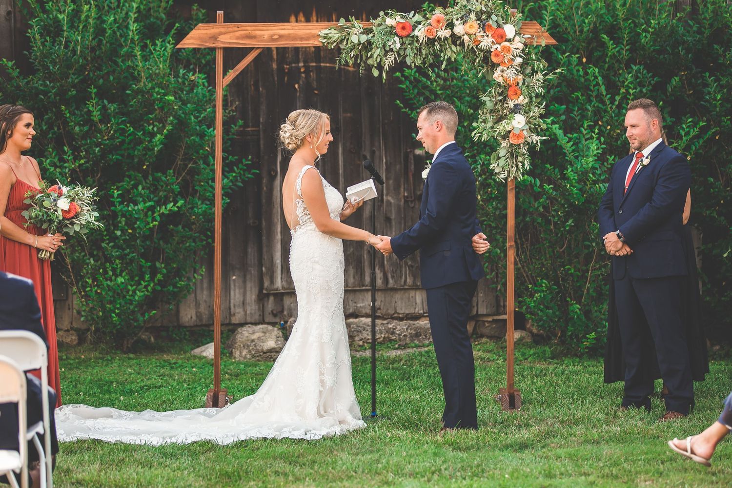 Wedding ceremony site with wooden arch and coral floral arrangements in a garden setting.