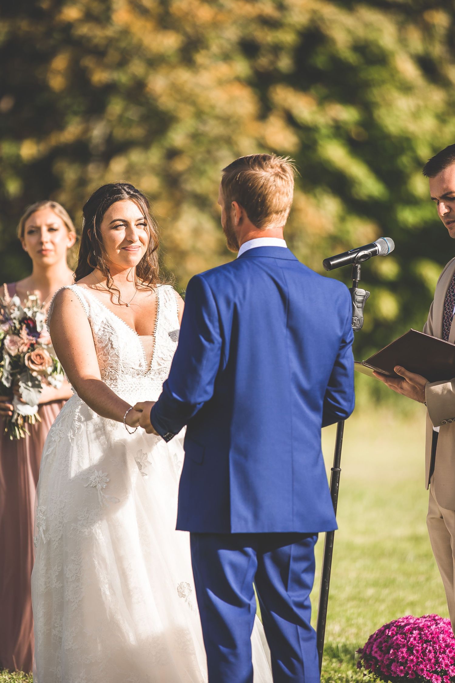 Outdoor wedding ceremony with officiant and wedding party against autumn foliage backdrop.