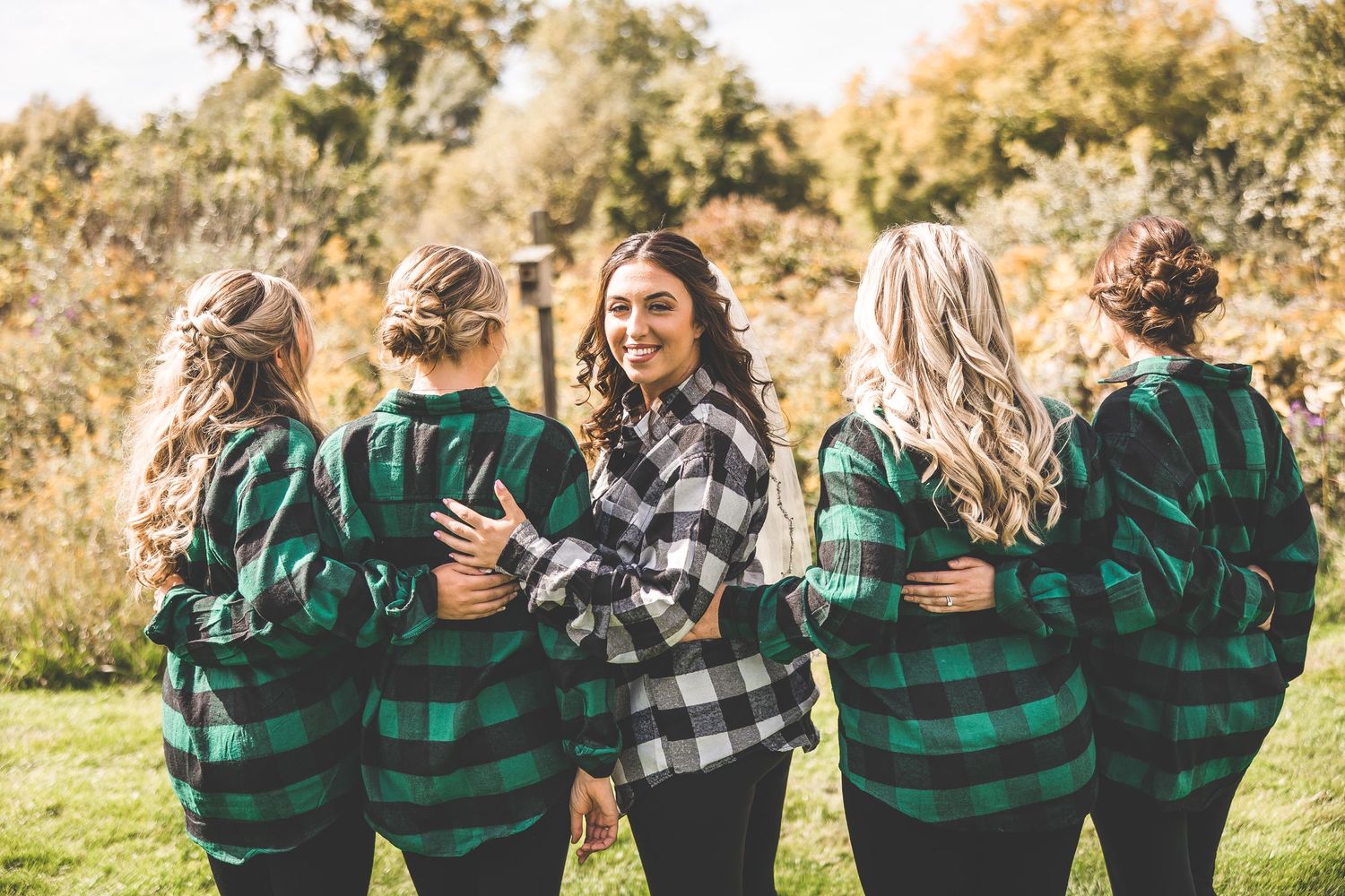 Group wearing coordinated buffalo plaid shirts embrace while laughing in autumn sunlight.