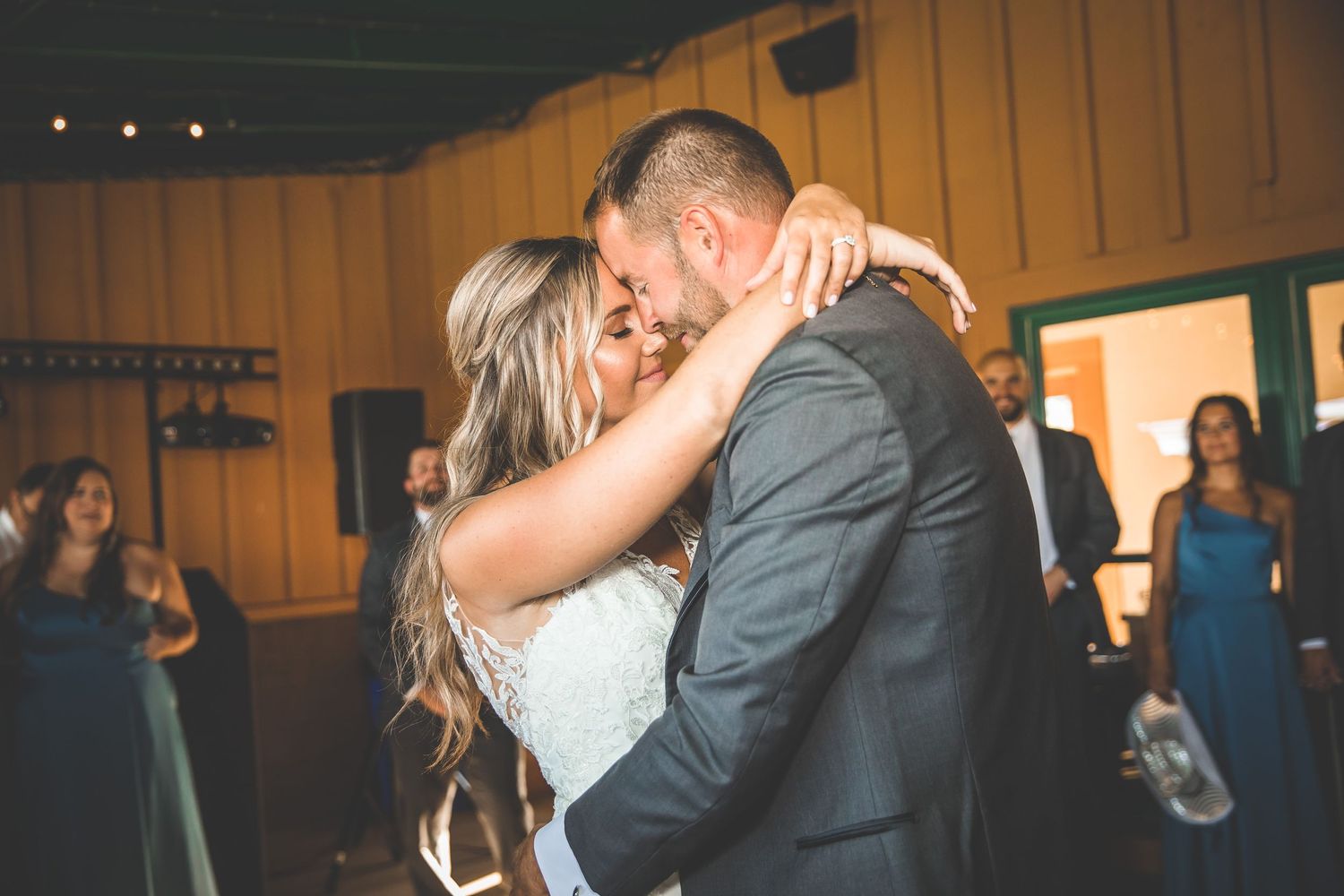 A couple embraces during their wedding dance in a warmly lit reception venue.