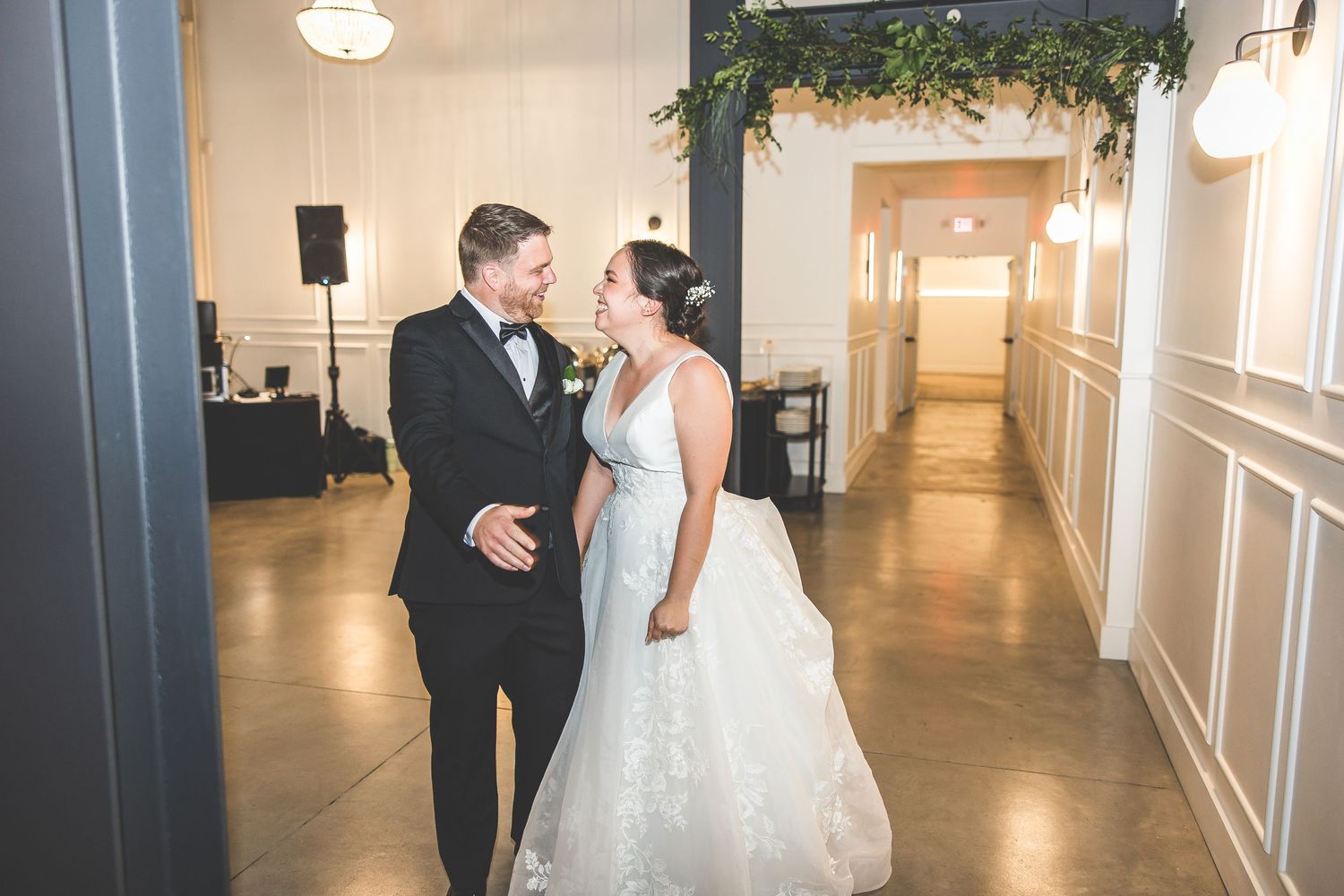 A couple shares their first dance in an elegant venue decorated with greenery and white walls.