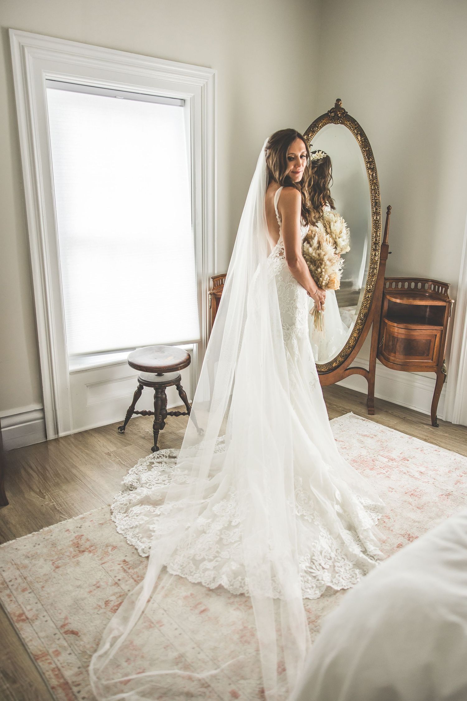 Wedding gown with long lace train displayed in sunlit room with antique furniture.