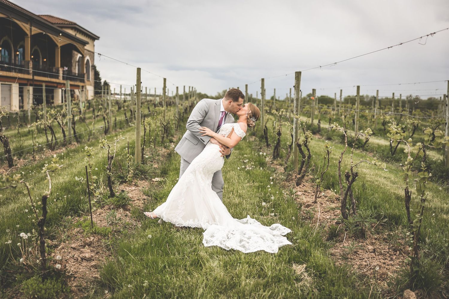 Wedding couple shares an intimate moment in a vineyard with trailing white dress and desert landscape.