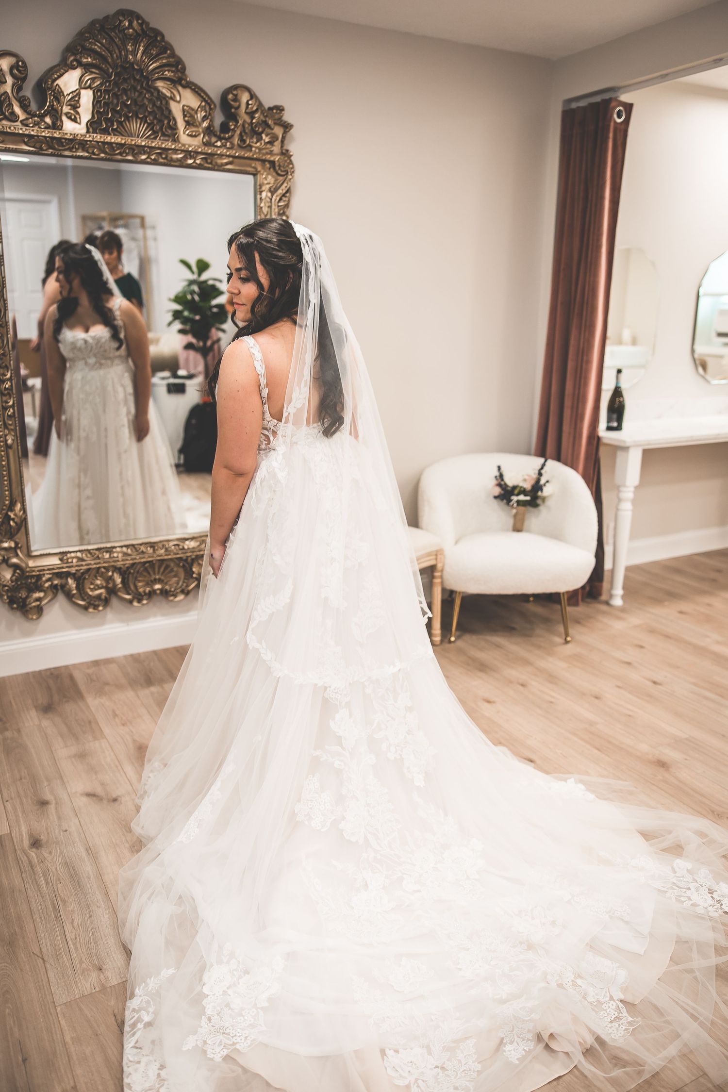 A flowing white wedding dress with intricate lace details and long train photographed in a bridal suite.