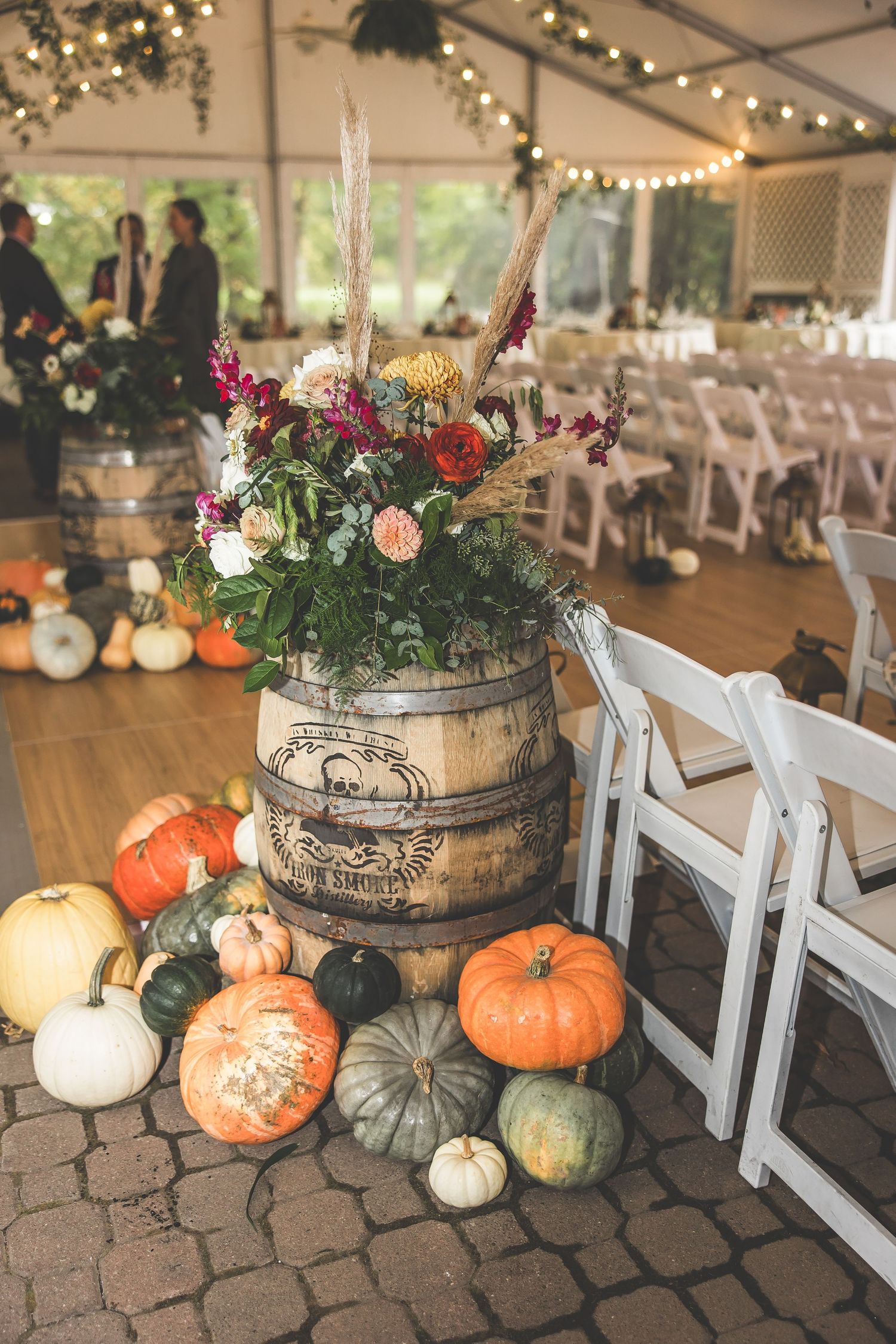 Rustic fall wedding decor featuring barrel vase with flowers surrounded by assorted pumpkins.