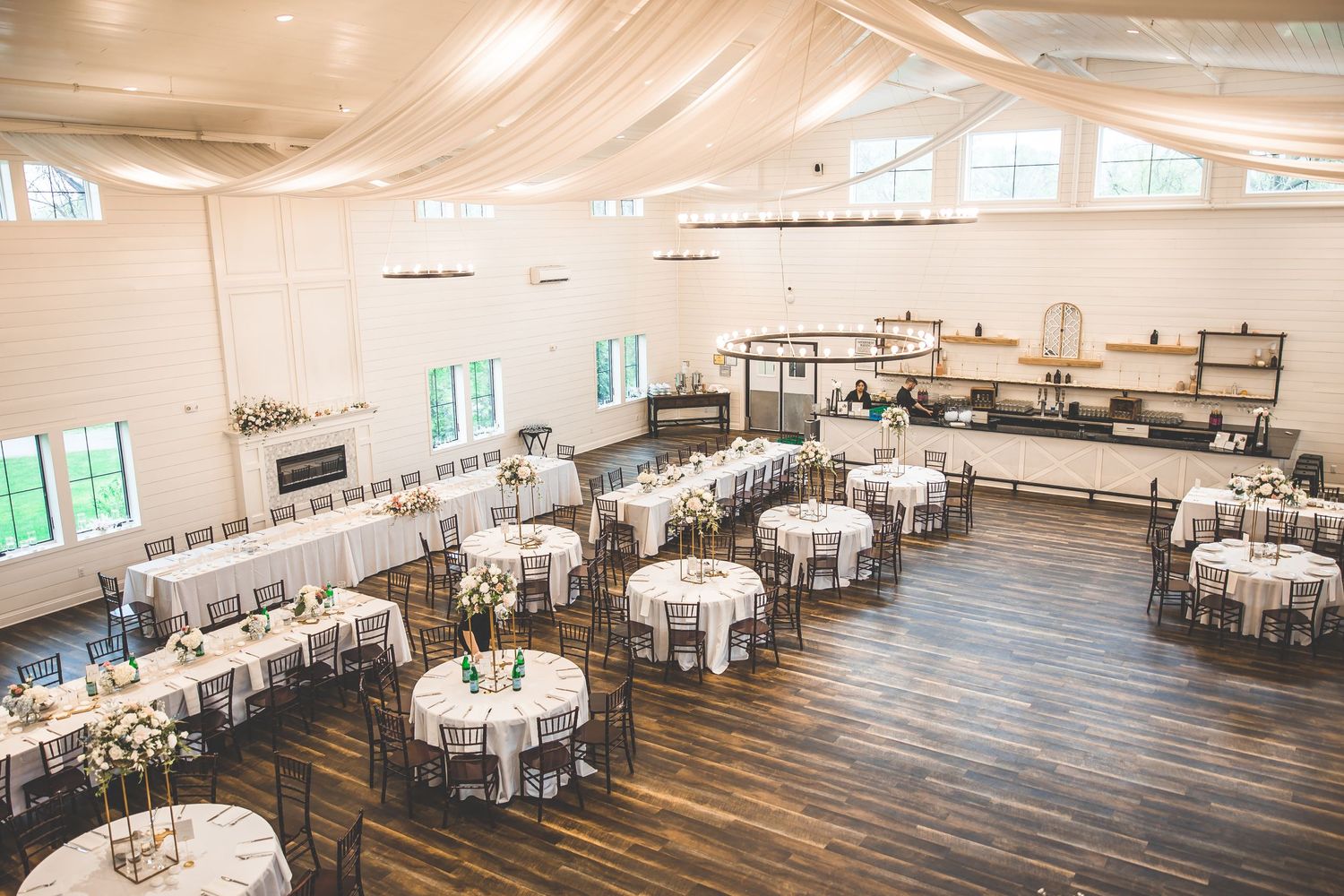 Large elegant wedding reception venue with white tablecloths and rustic wooden floors.