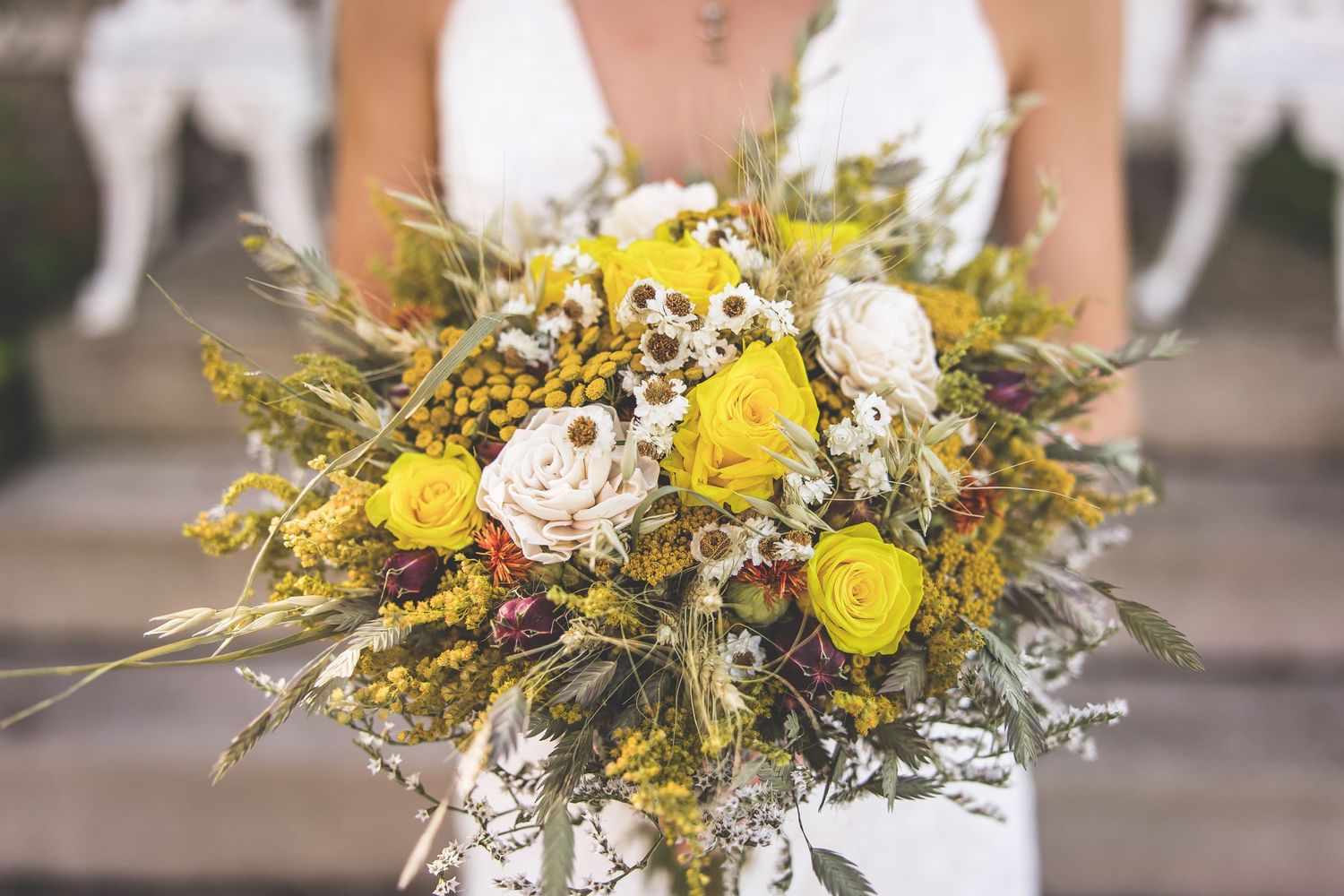 A detailed shot of a rustic wedding bouquet featuring yellow roses and white flowers with natural greenery.