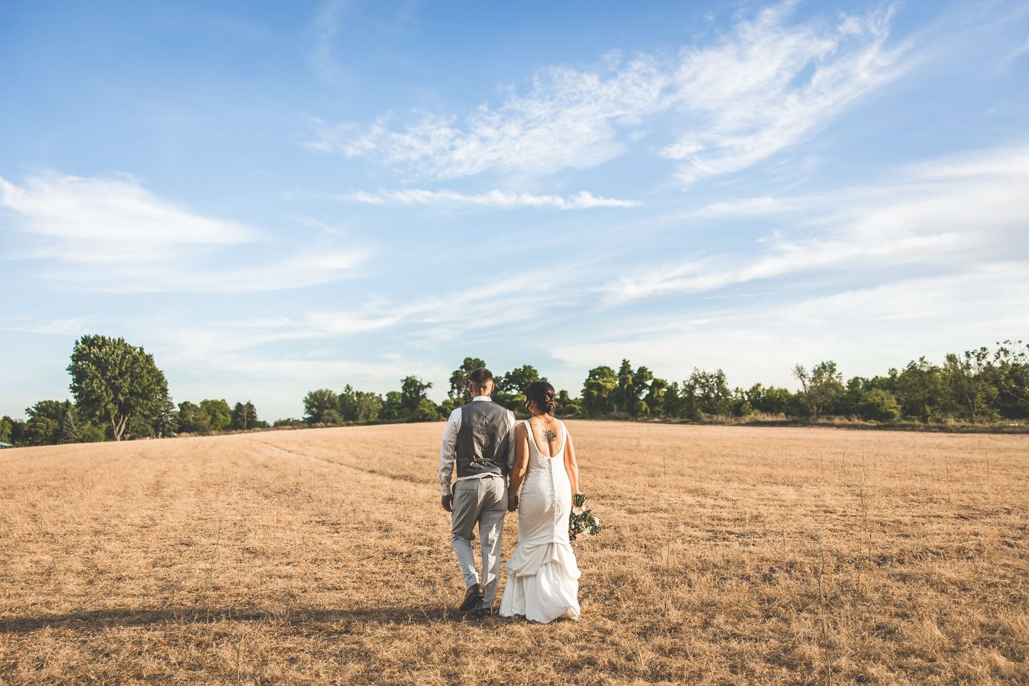 Panoramic view of a couple walking through a golden field at sunset after their wedding.