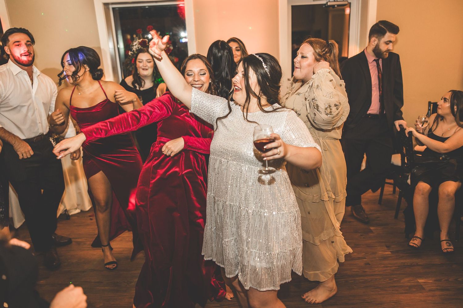 Wedding reception guests dancing in formal attire on wooden dance floor.