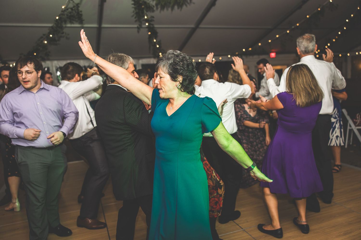 Wedding celebration showing guests dancing in colorful dresses under string lights at an indoor reception.