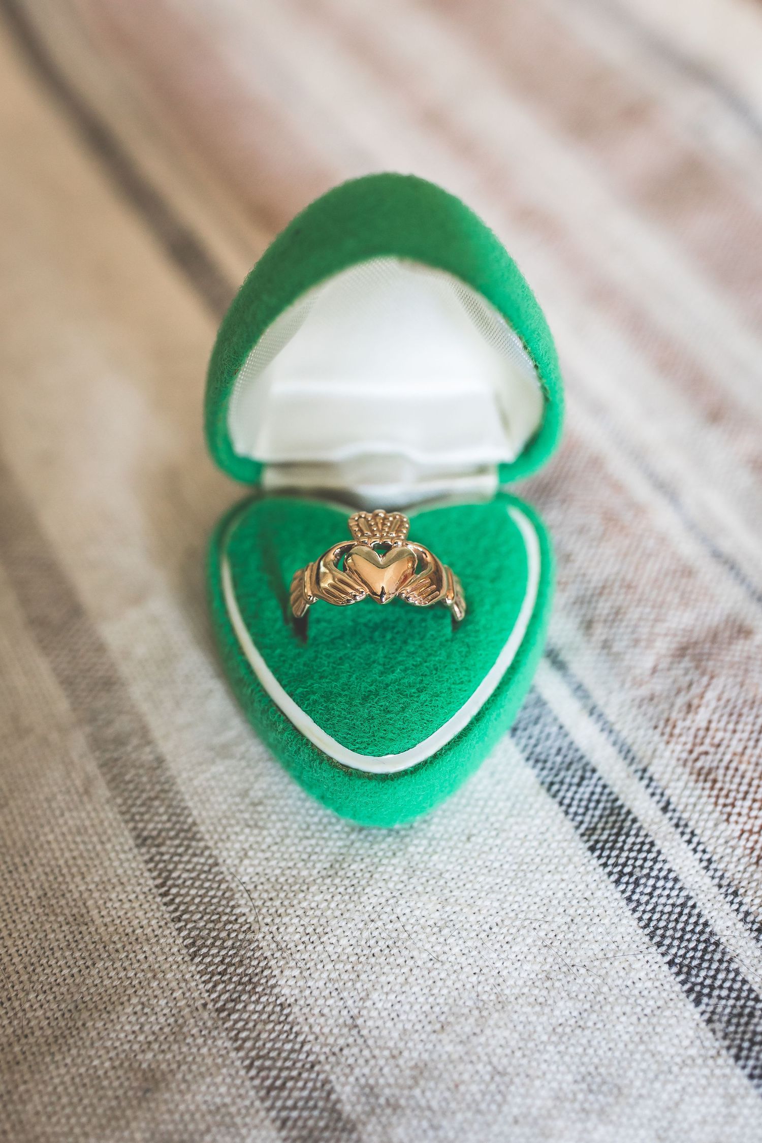 A delicate gold ring sits in an emerald green velvet ring box on textured fabric.
