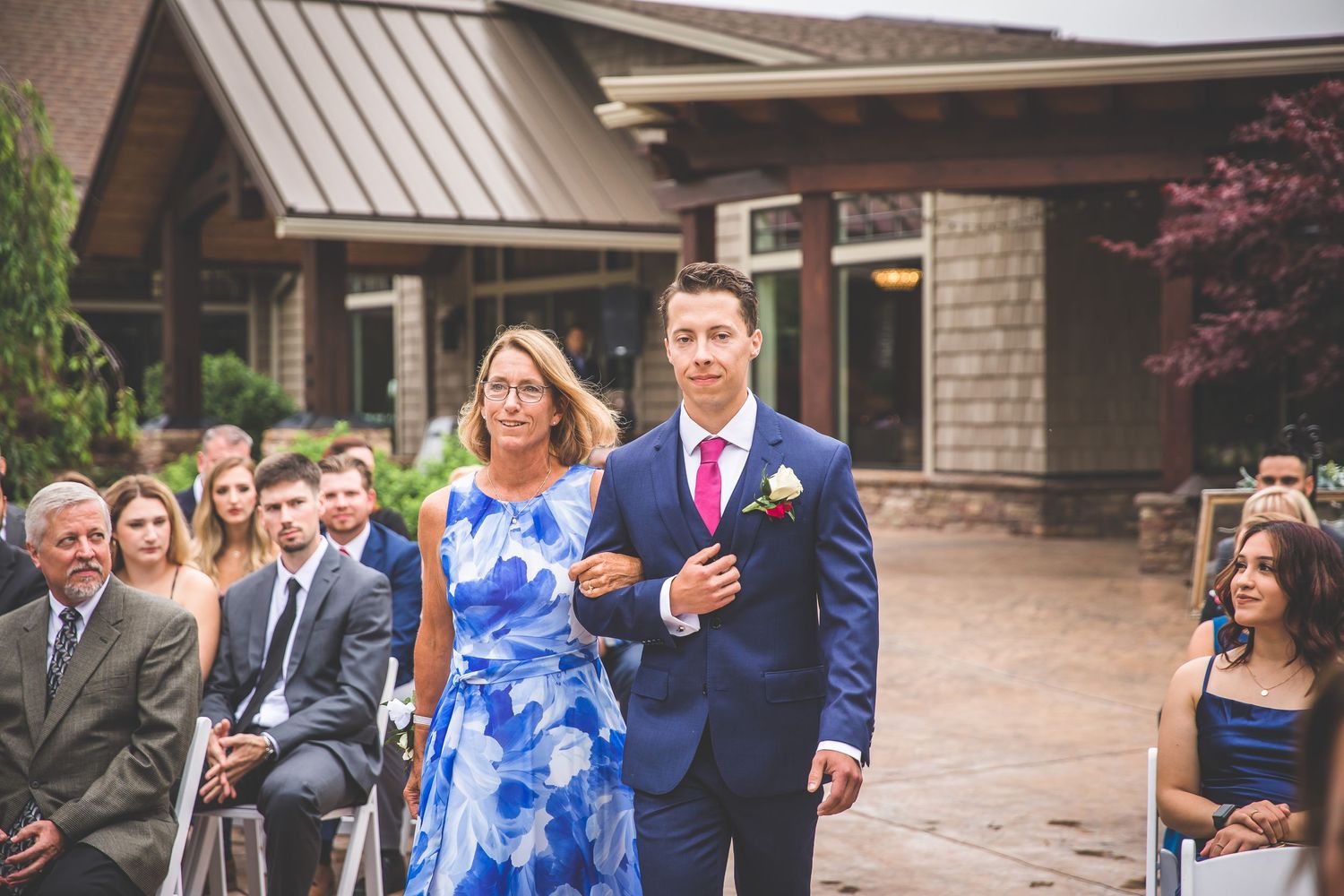 Wedding ceremony guests seated in white chairs on a paved outdoor courtyard.
