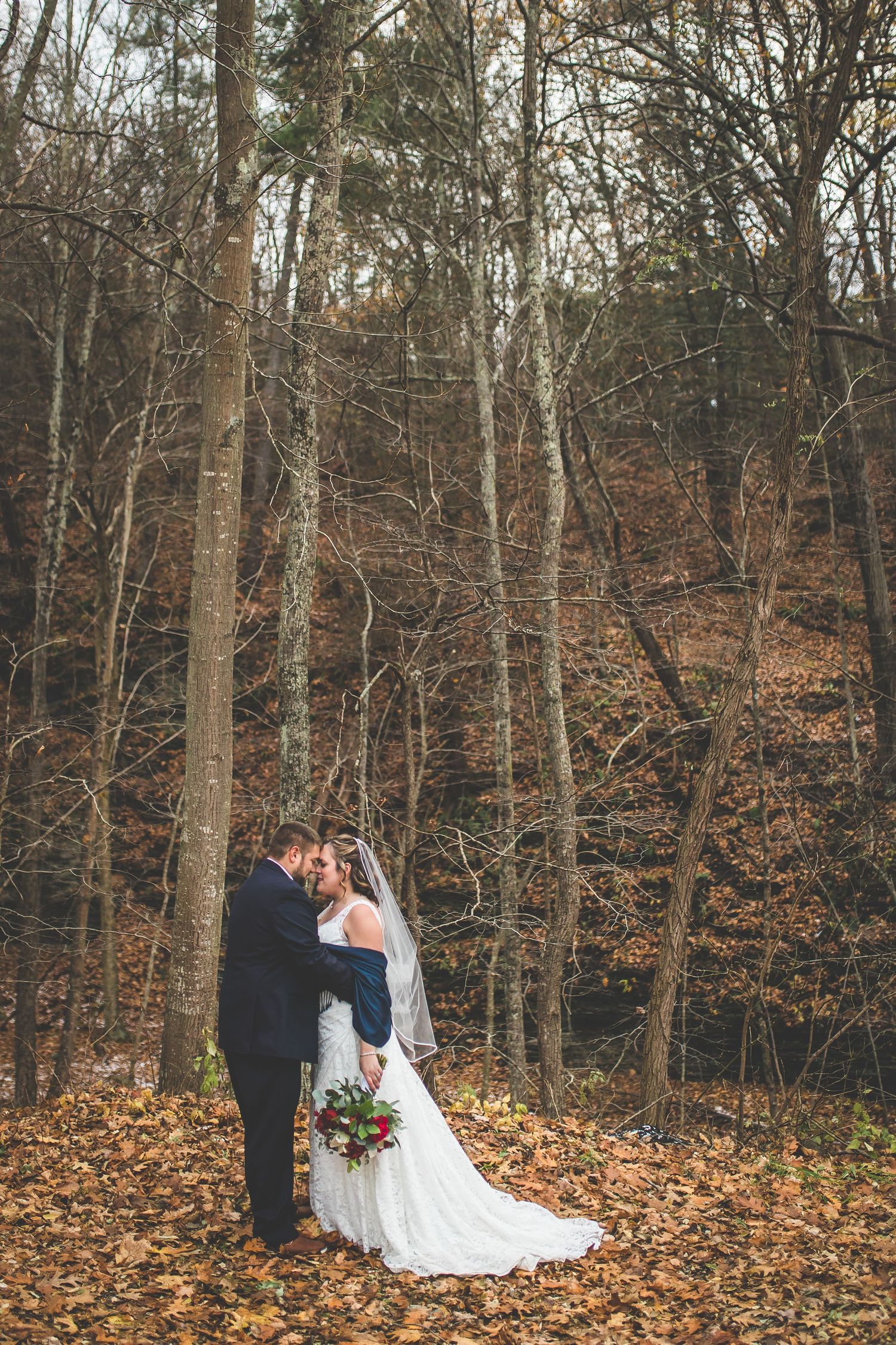 Romantic autumn wedding photos among bare trees with fallen leaves.