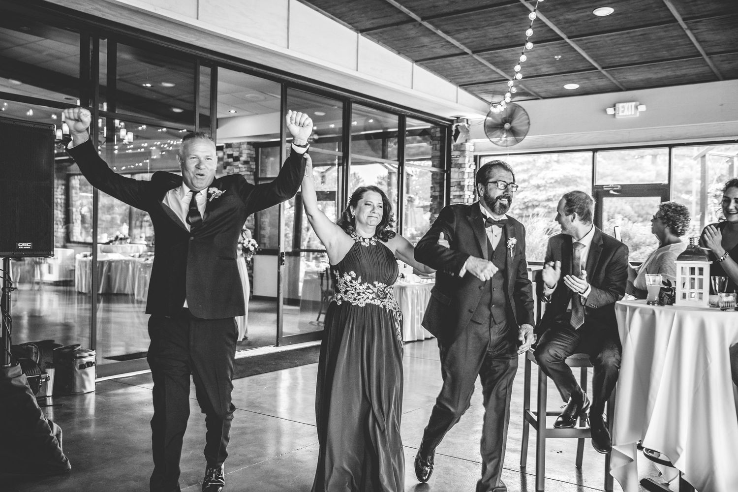 Wedding guests dancing and celebrating in a modern reception venue with floor-to-ceiling windows.