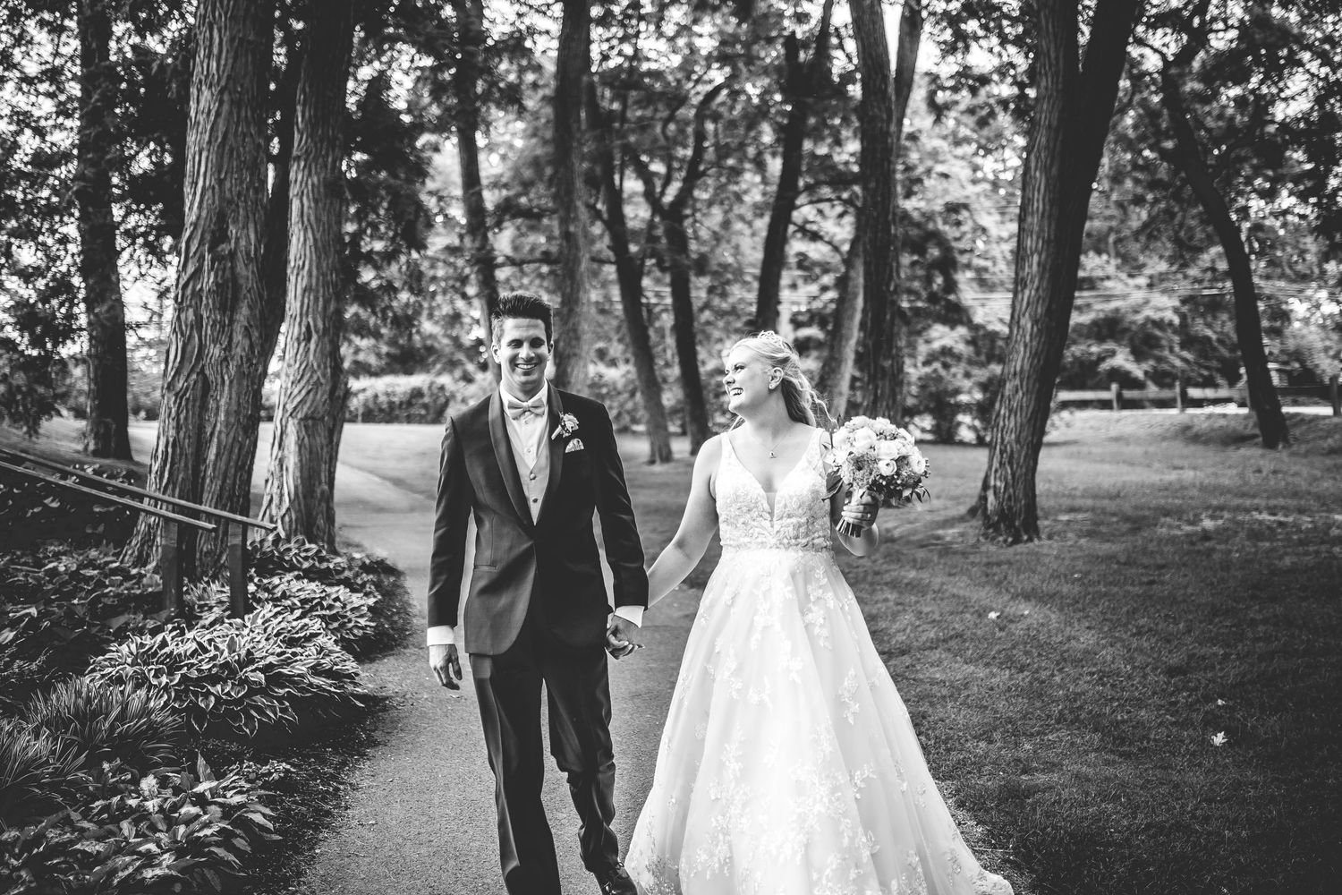 Black and white photo of newlyweds walking together along a scenic garden path.