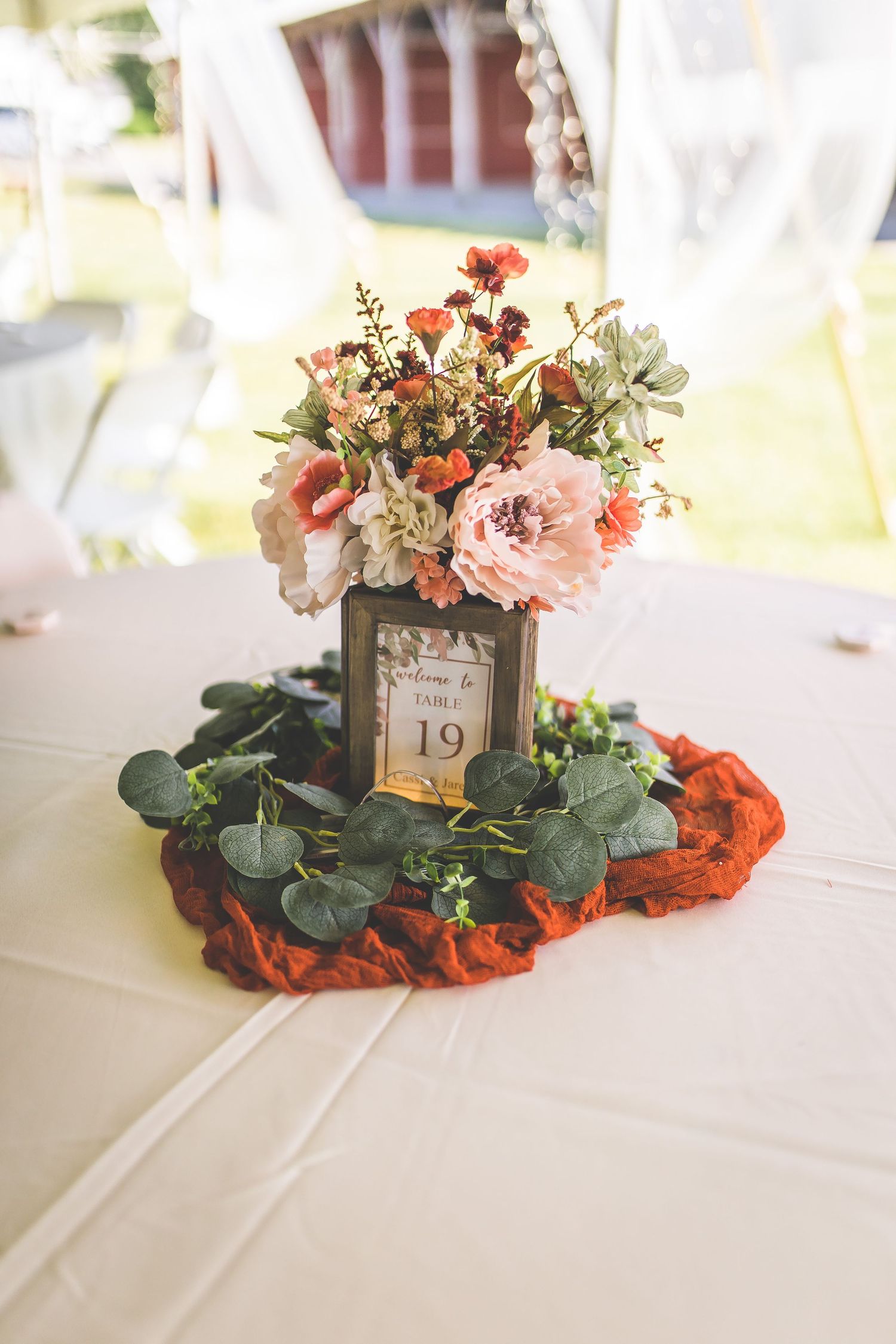Elegant wedding table centerpiece with pink flowers and eucalyptus on white linens.