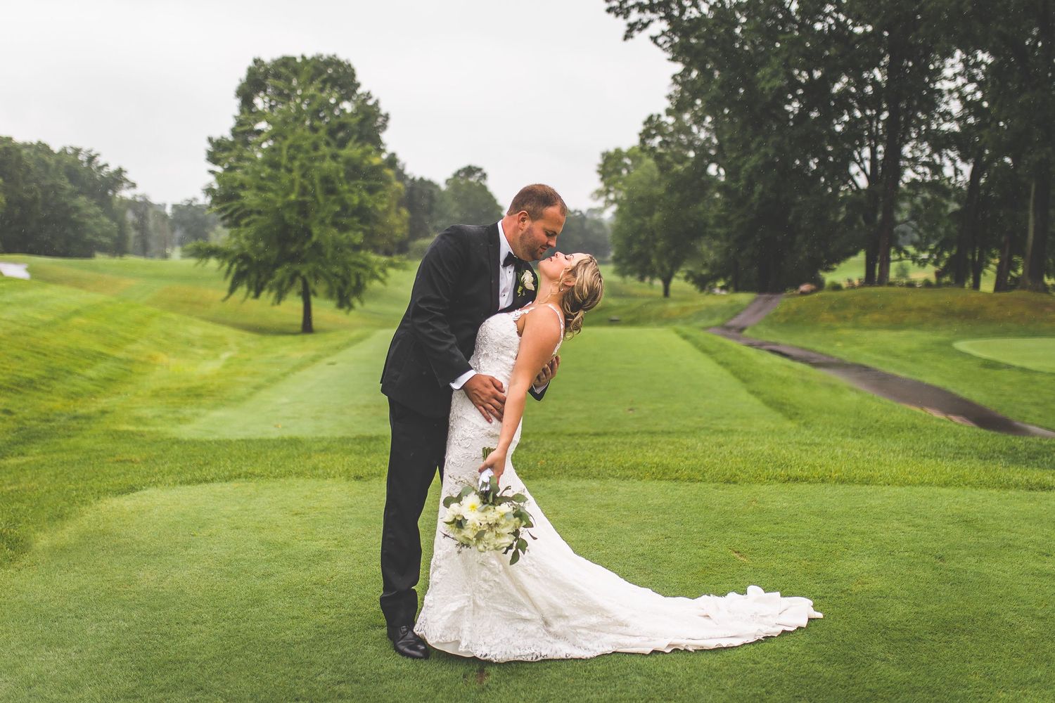Wedding couple poses romantically on lush green golf course fairway.