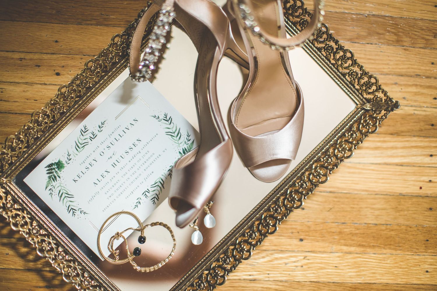 Wedding invitation and blush heels arranged on ornate gold tray with wedding rings.