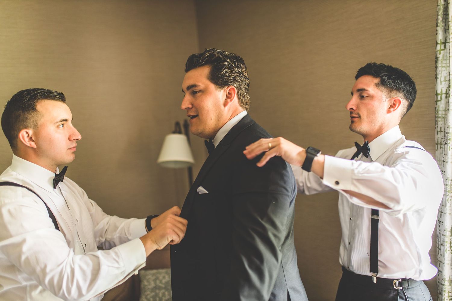 Groomsmen helping each other get dressed in white shirts and formal attire.