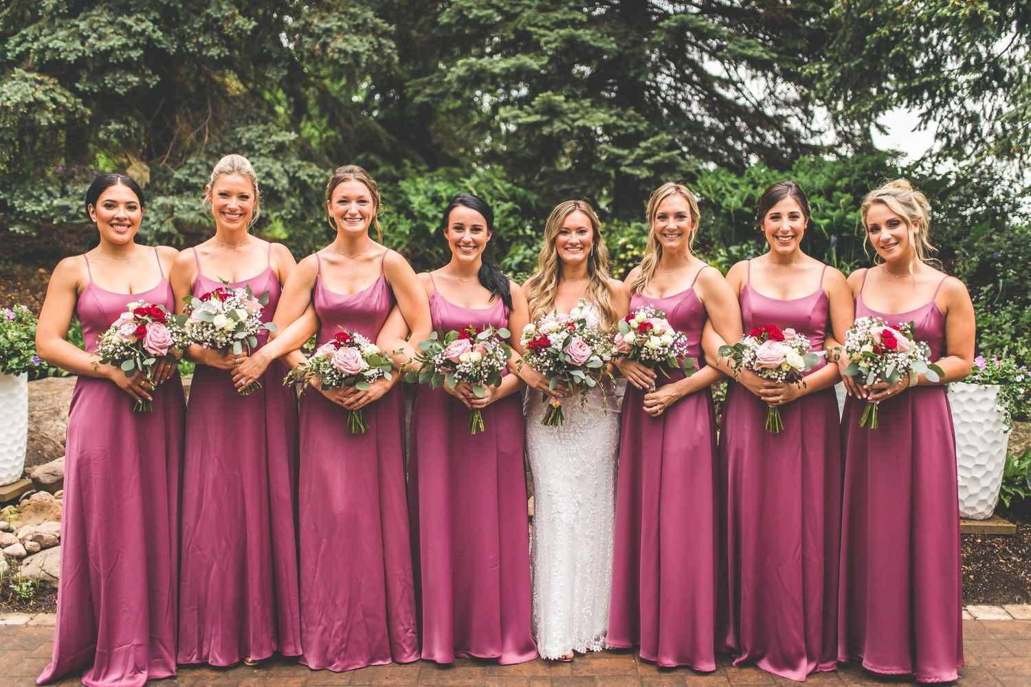 Bridal party with bridesmaids wearing matching dusty rose gowns holding pink and white bouquets.