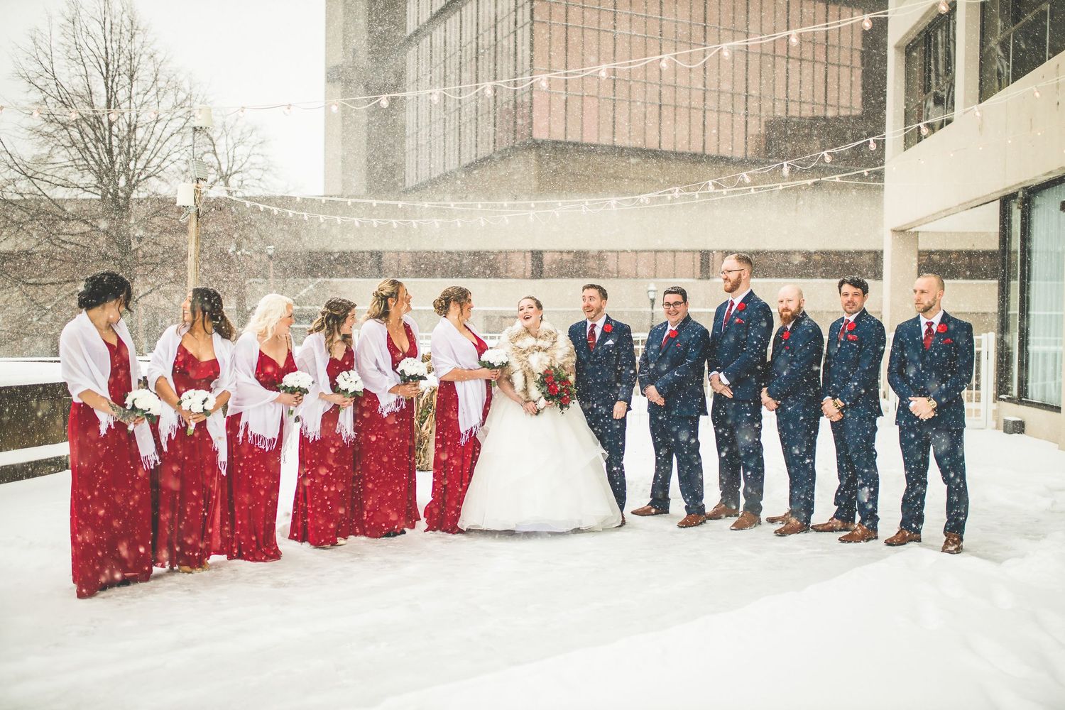 Wedding party lined up outdoors in winter with bridesmaids in red and groomsmen in navy suits.