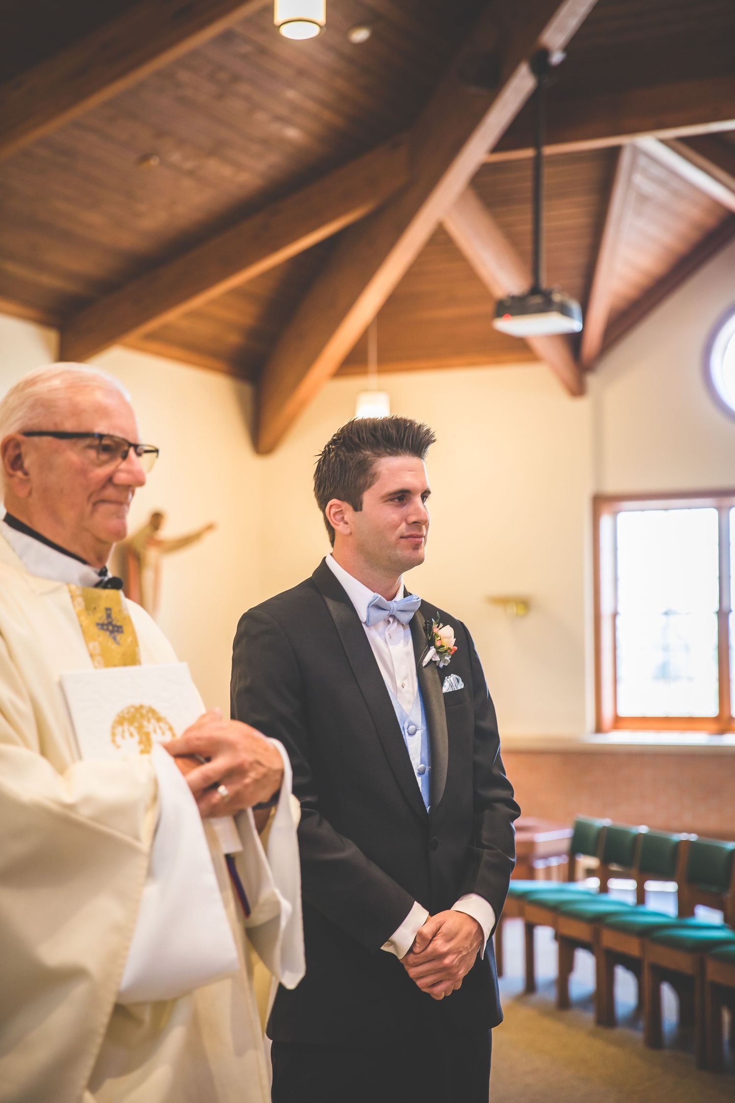 Groom and groomsmen stand at altar in church with wooden beamed ceiling.