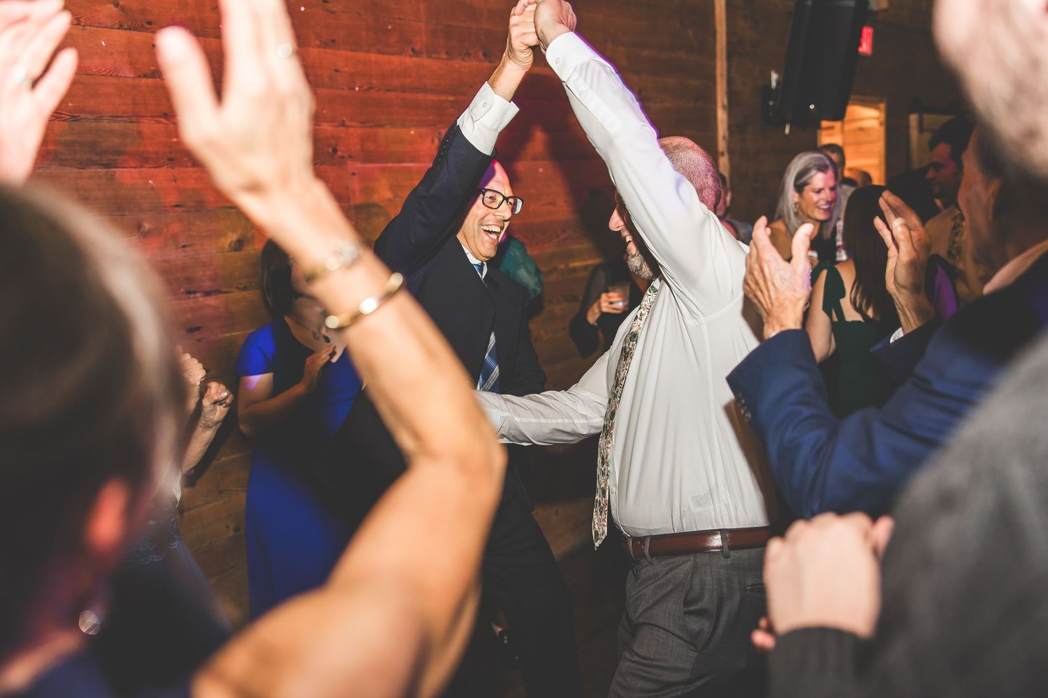 Crowd raises hands in celebration during wedding reception dance party.
